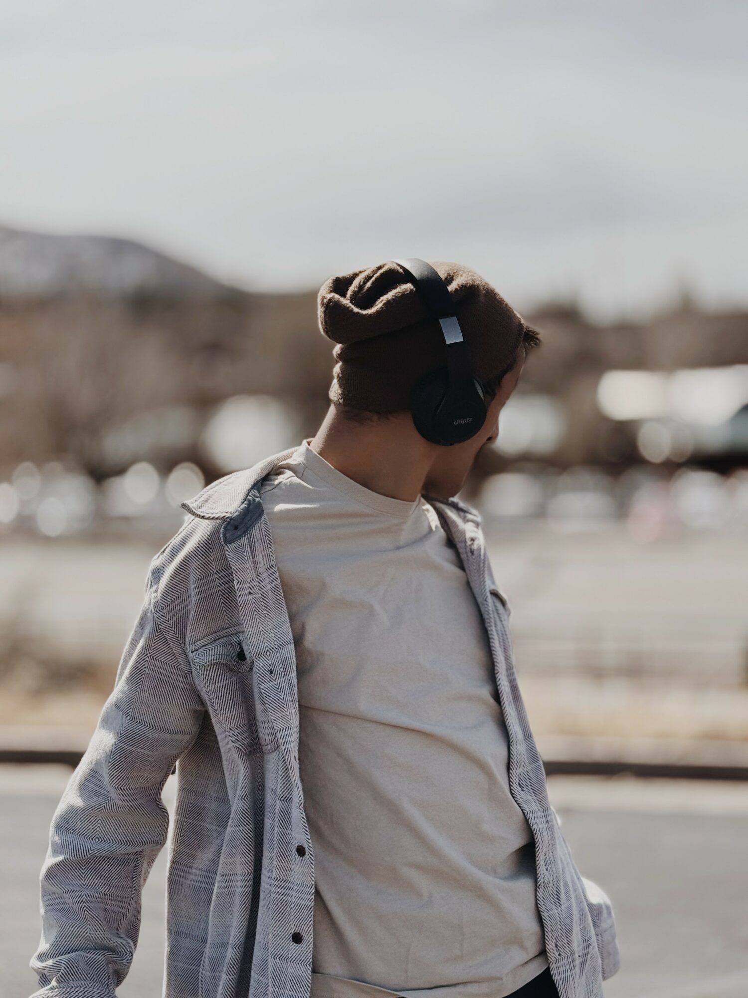 Person wearing headphones and a beanie, looking down, outdoors with blurred background.