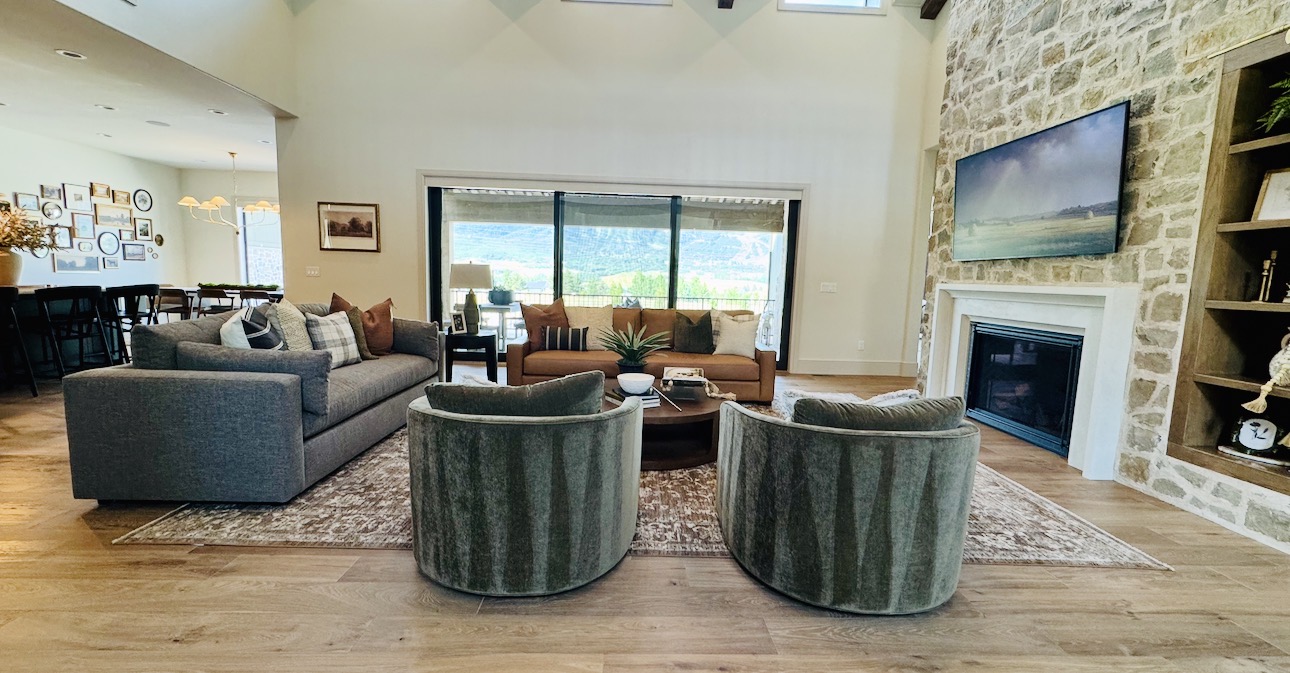 Living room with two green armchairs, a gray sofa, a fireplace, and a large window with a view outside.