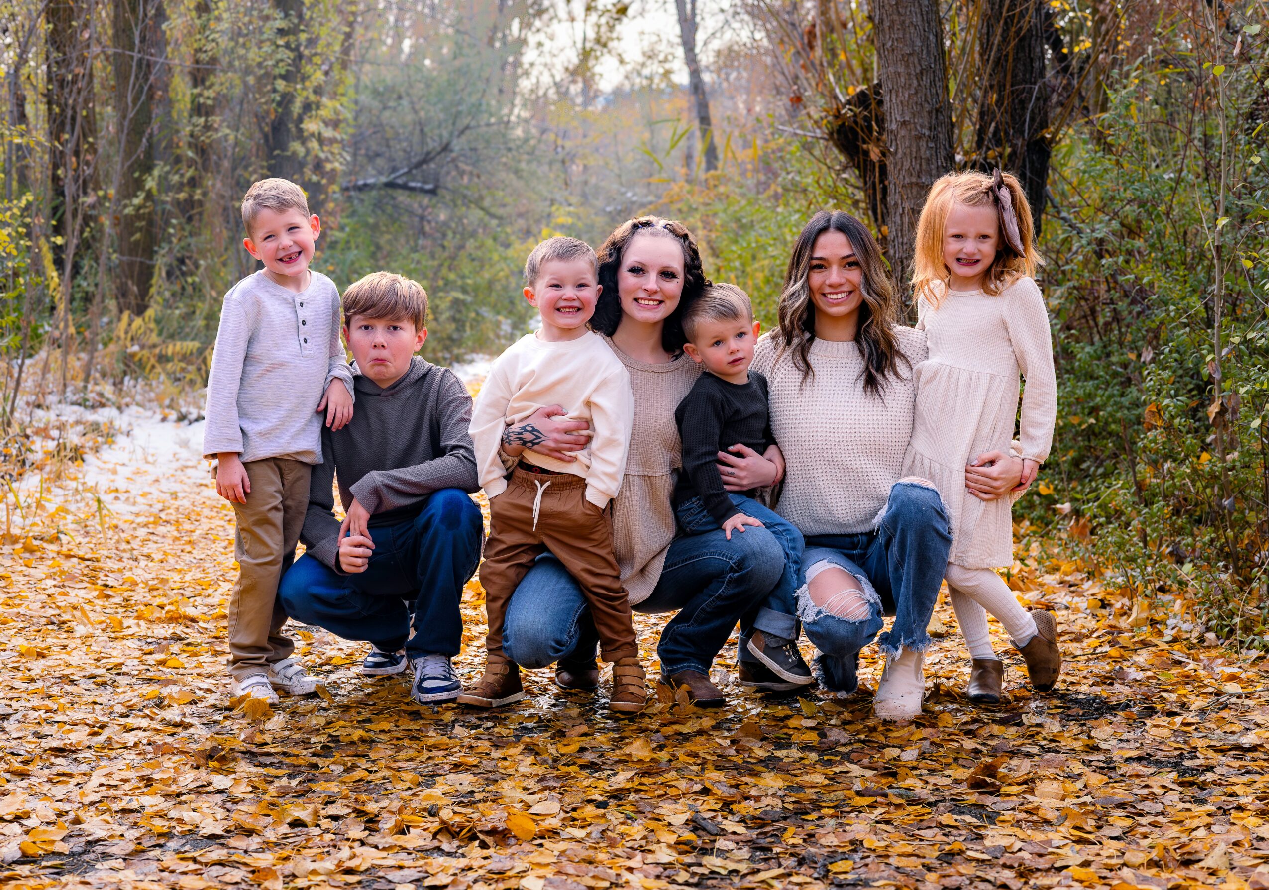 Group of seven people, including children and adults, standing outdoors on fallen leaves in a wooded area.