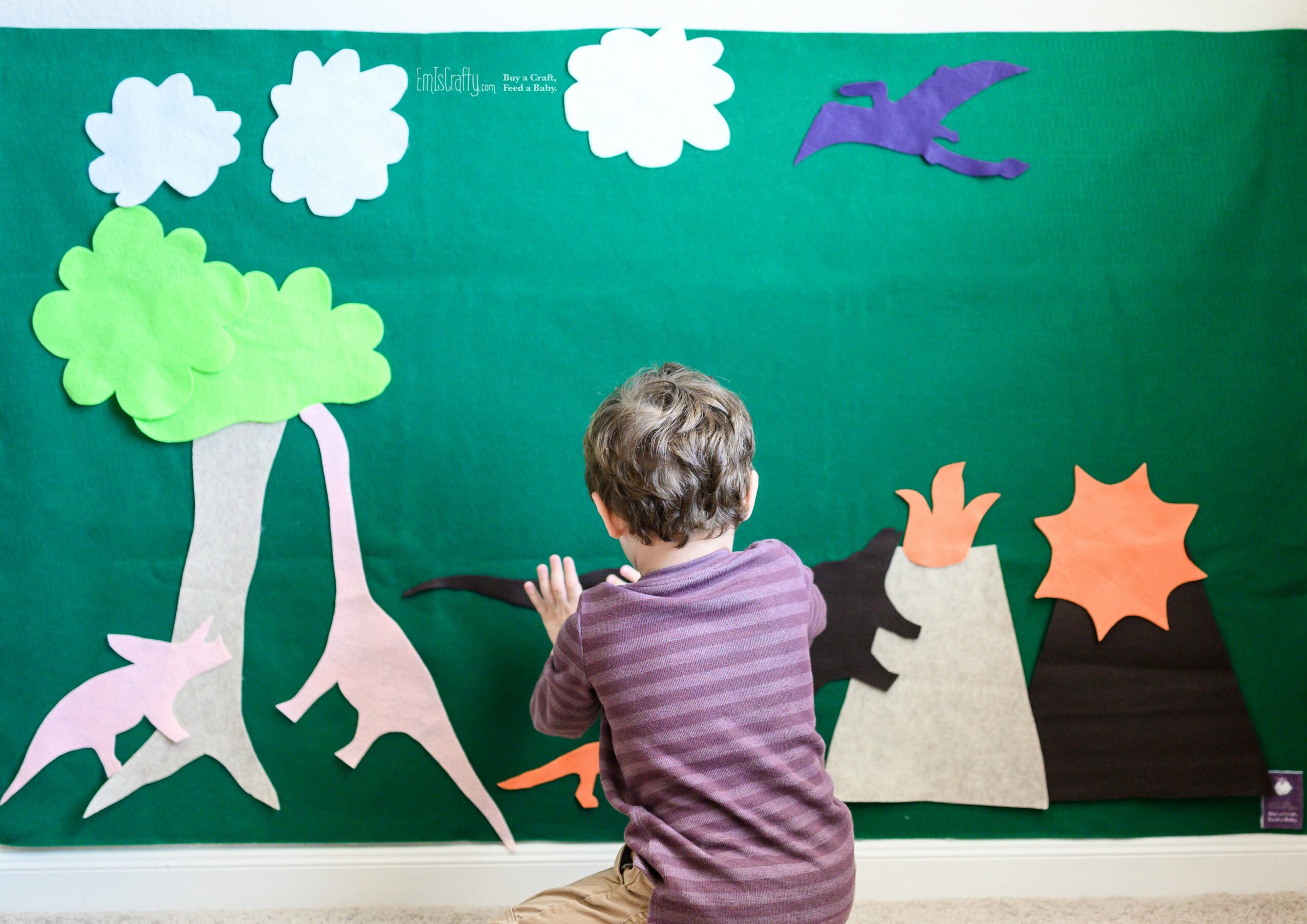 Child with curly hair facing a green background with paper trees, clouds, a bird, and mountains.