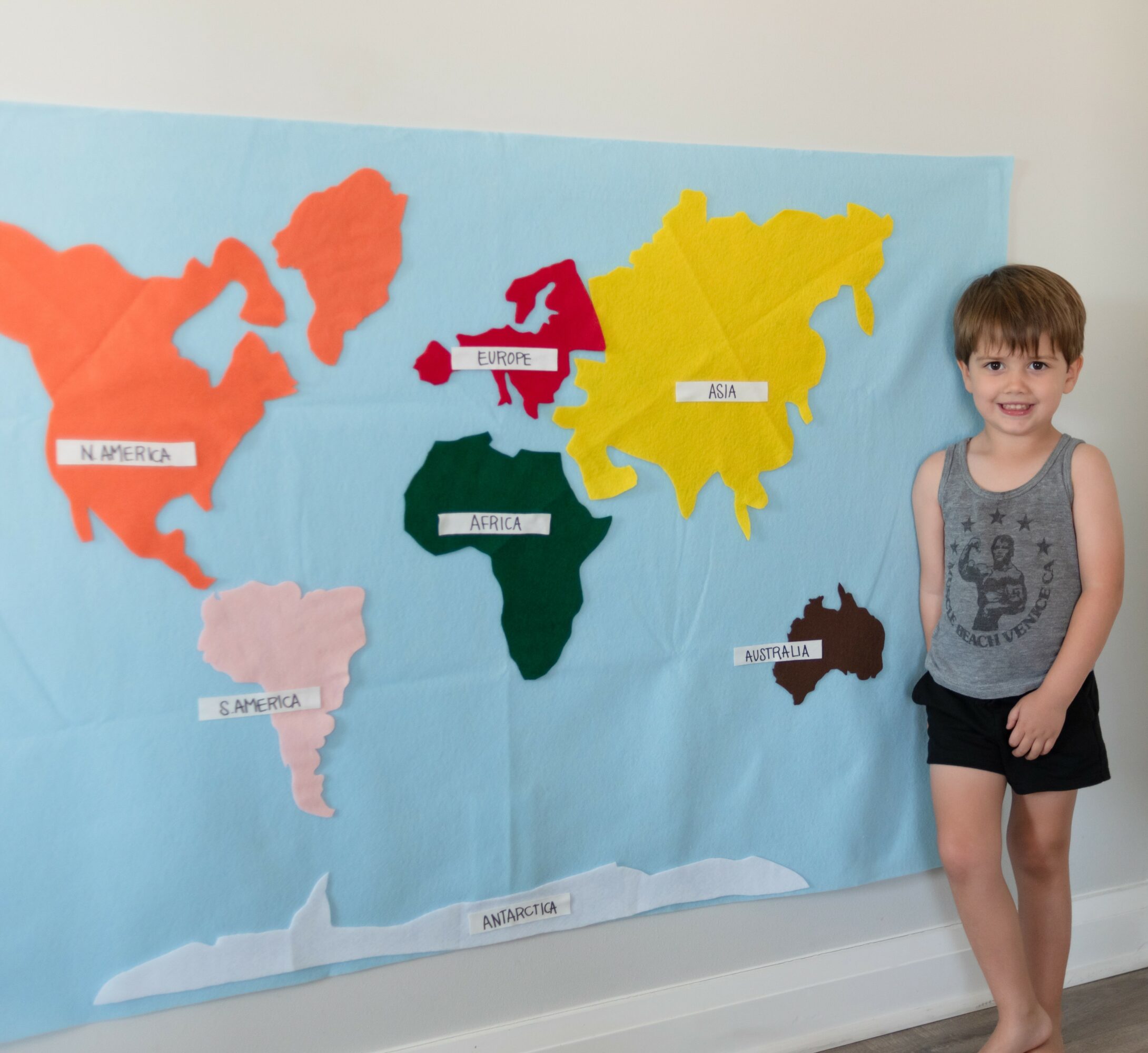 Child standing next to a colorful world map with country labels on a wall.