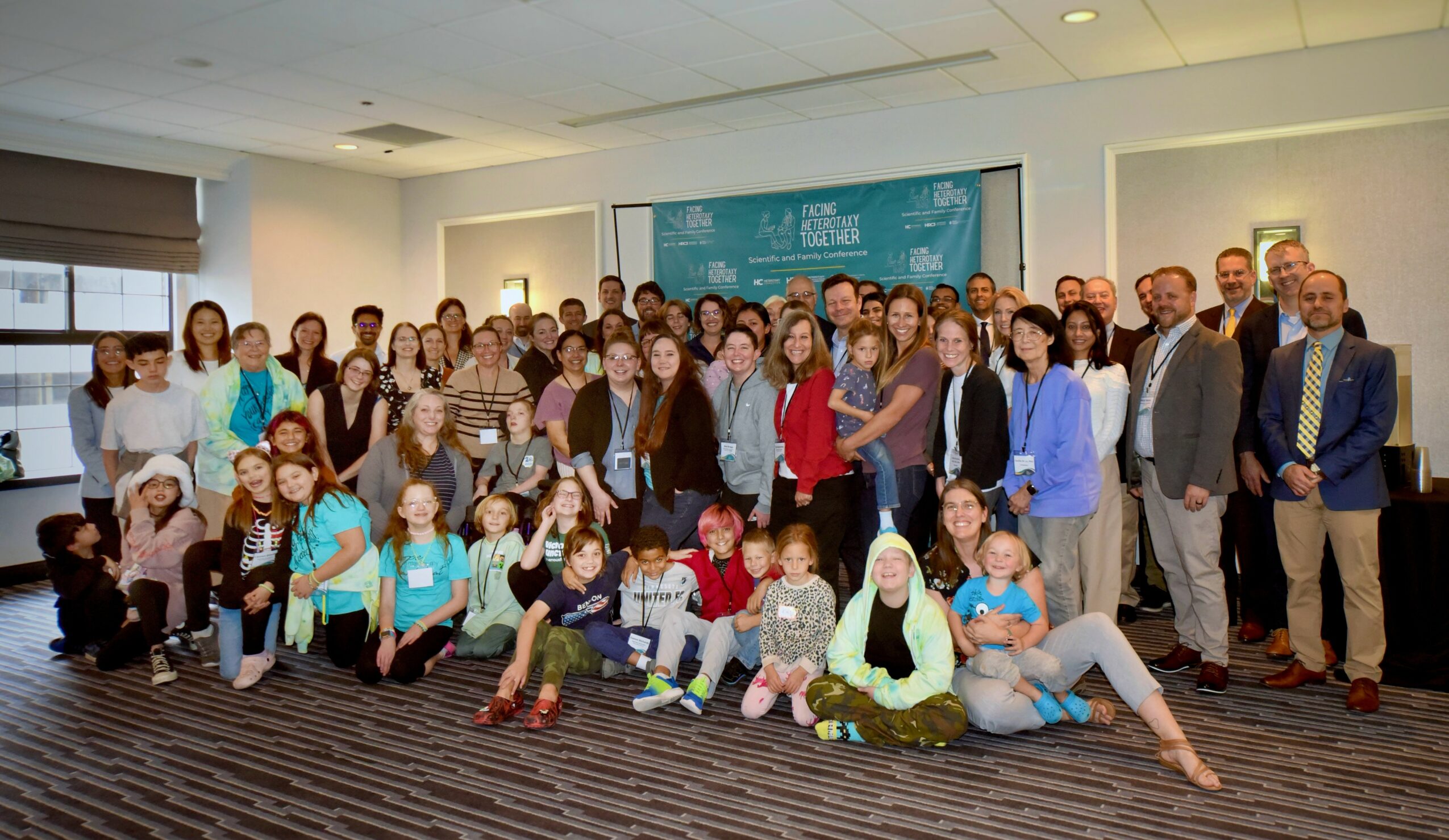 Group of diverse people posing in a conference room, some sitting and some standing, with a blue backdrop.