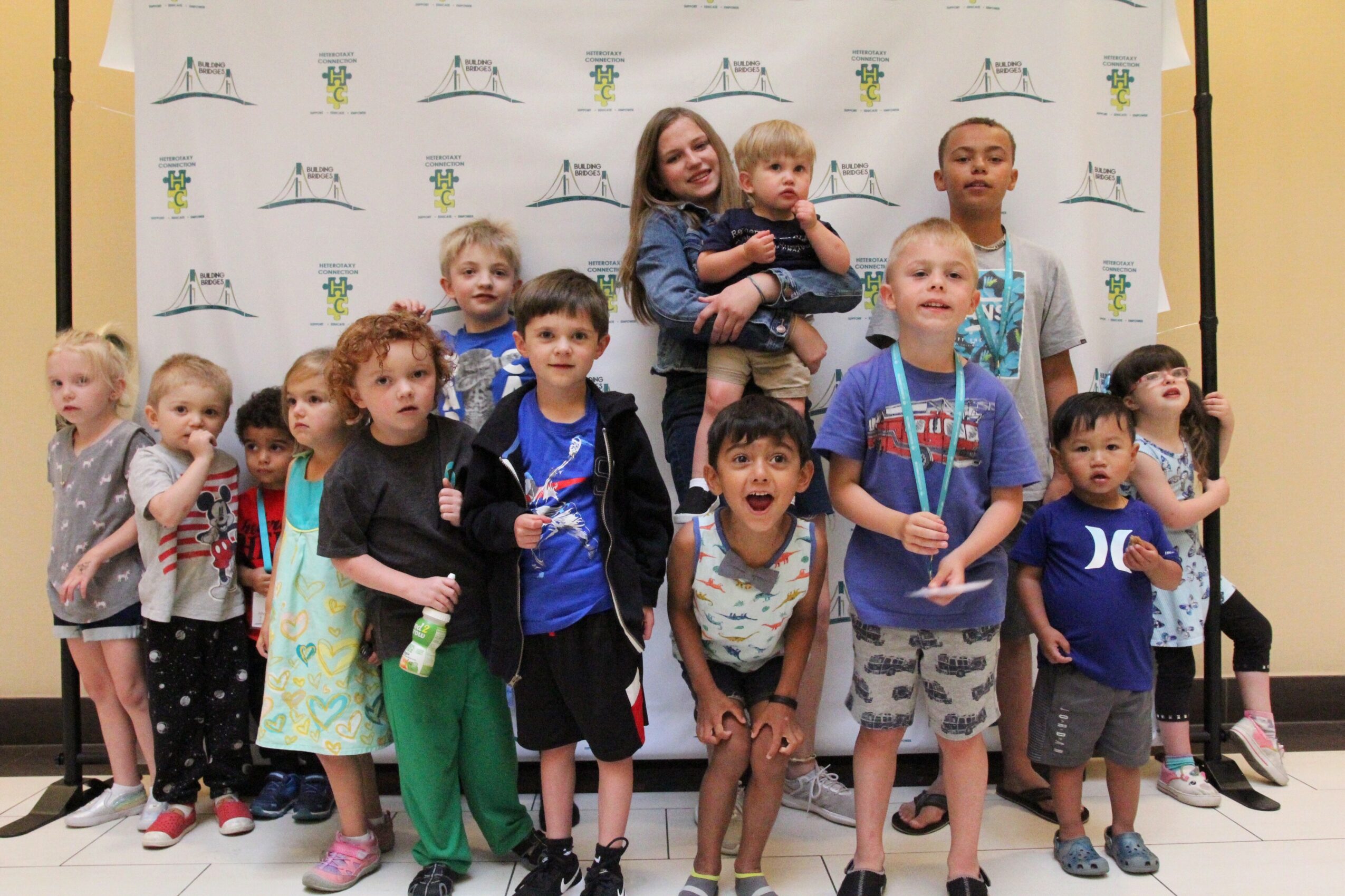Group of children and two adults standing in front of a backdrop with logos, some children holding medals and toys.