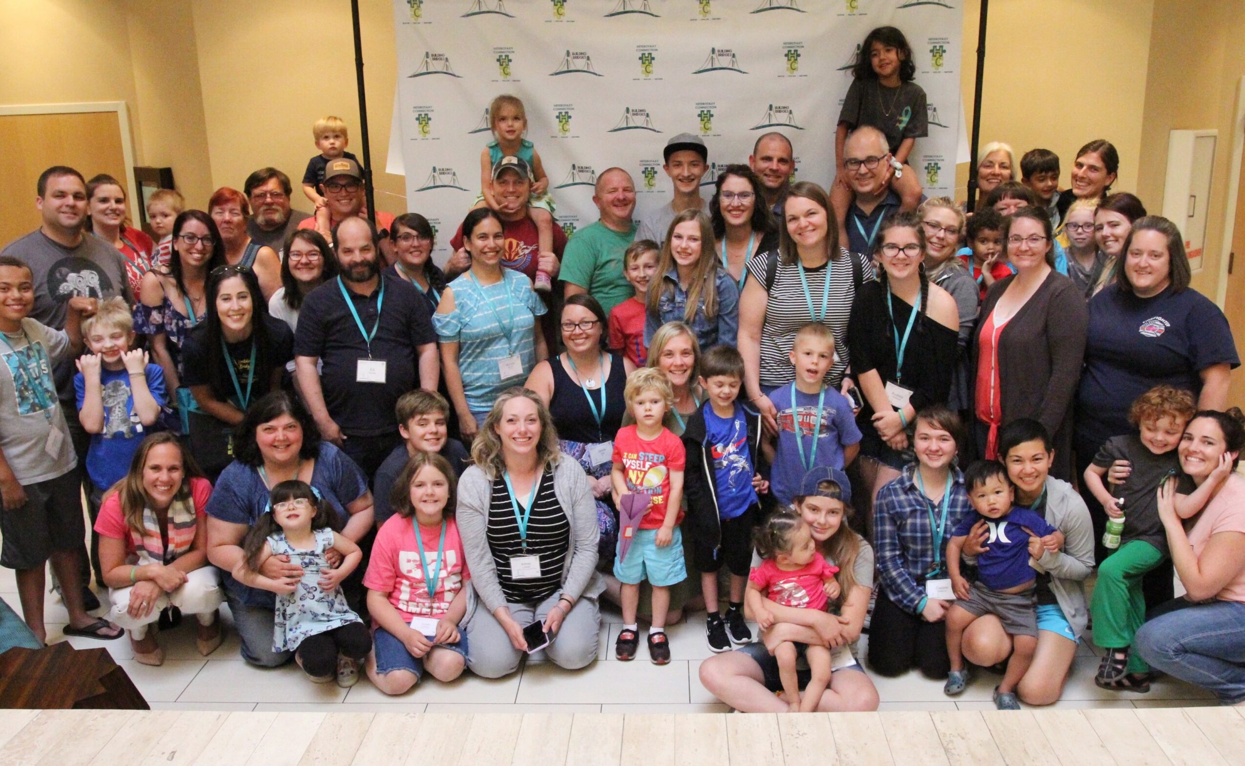 Group of children and adults posing indoors in front of a backdrop with logos.