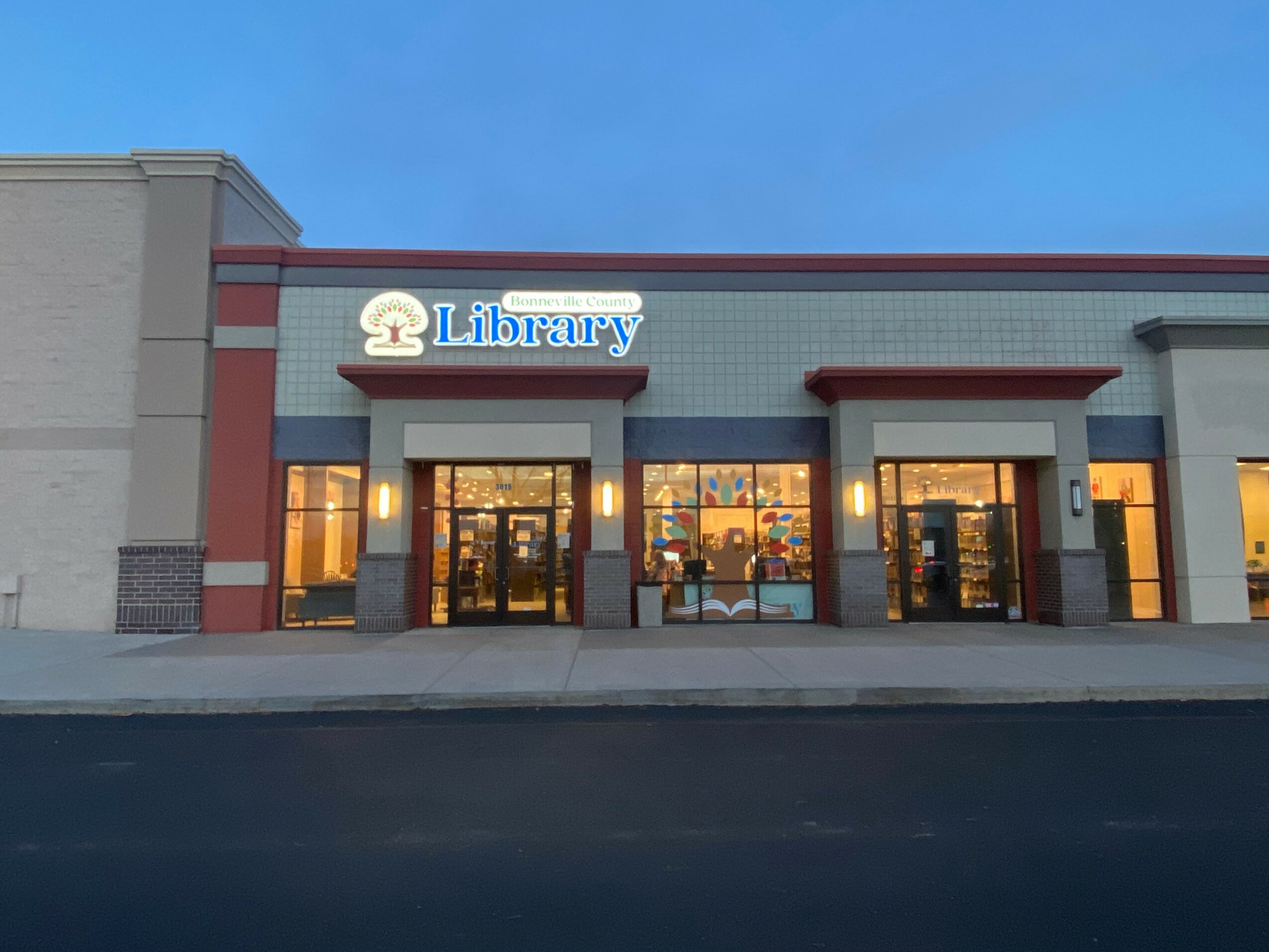 Library building with glass doors and windows, sign reading 'Library' on the facade, under a clear blue sky.