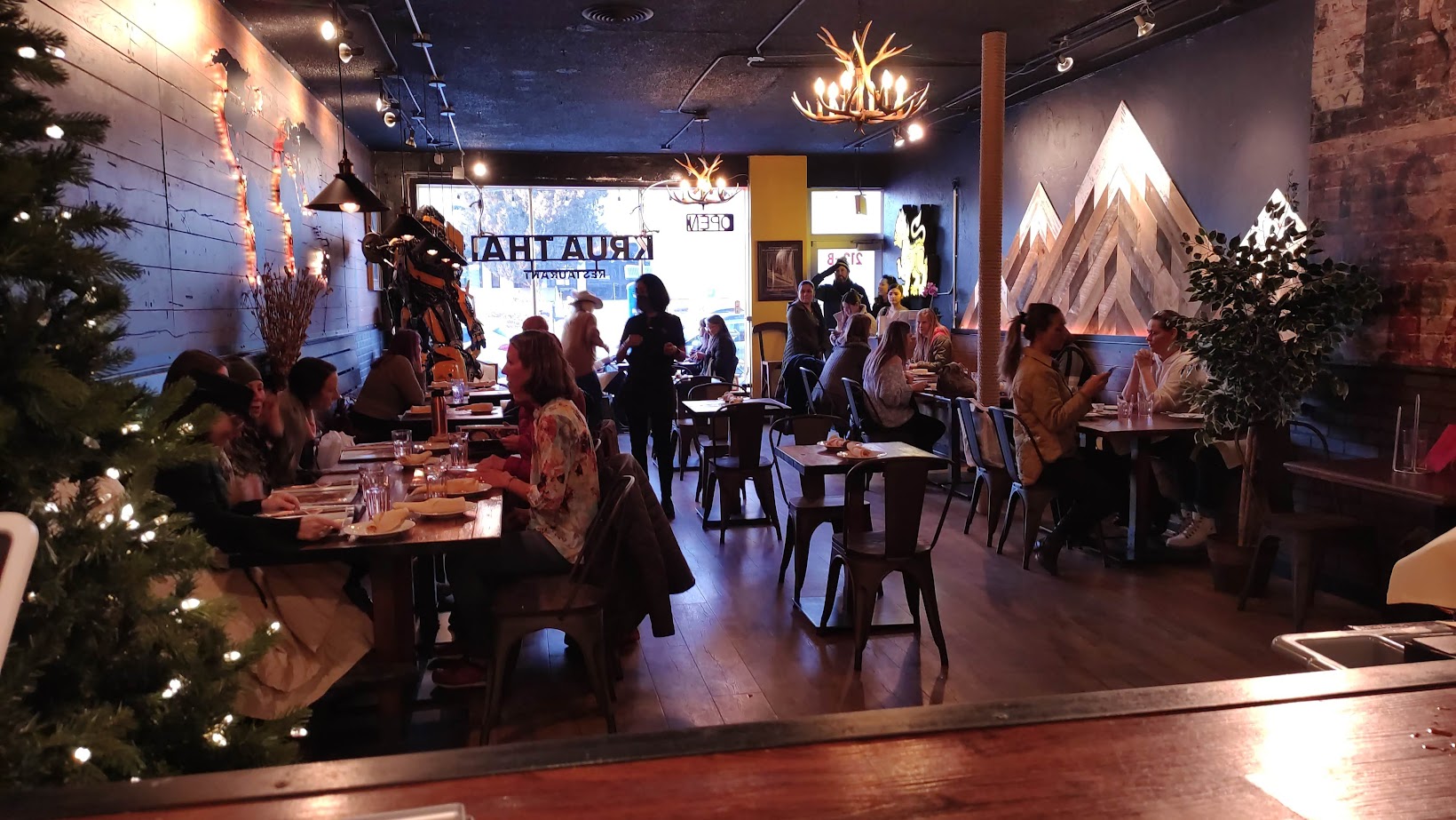 People dining in a cozy restaurant with Christmas decorations and a large window showing a street scene.