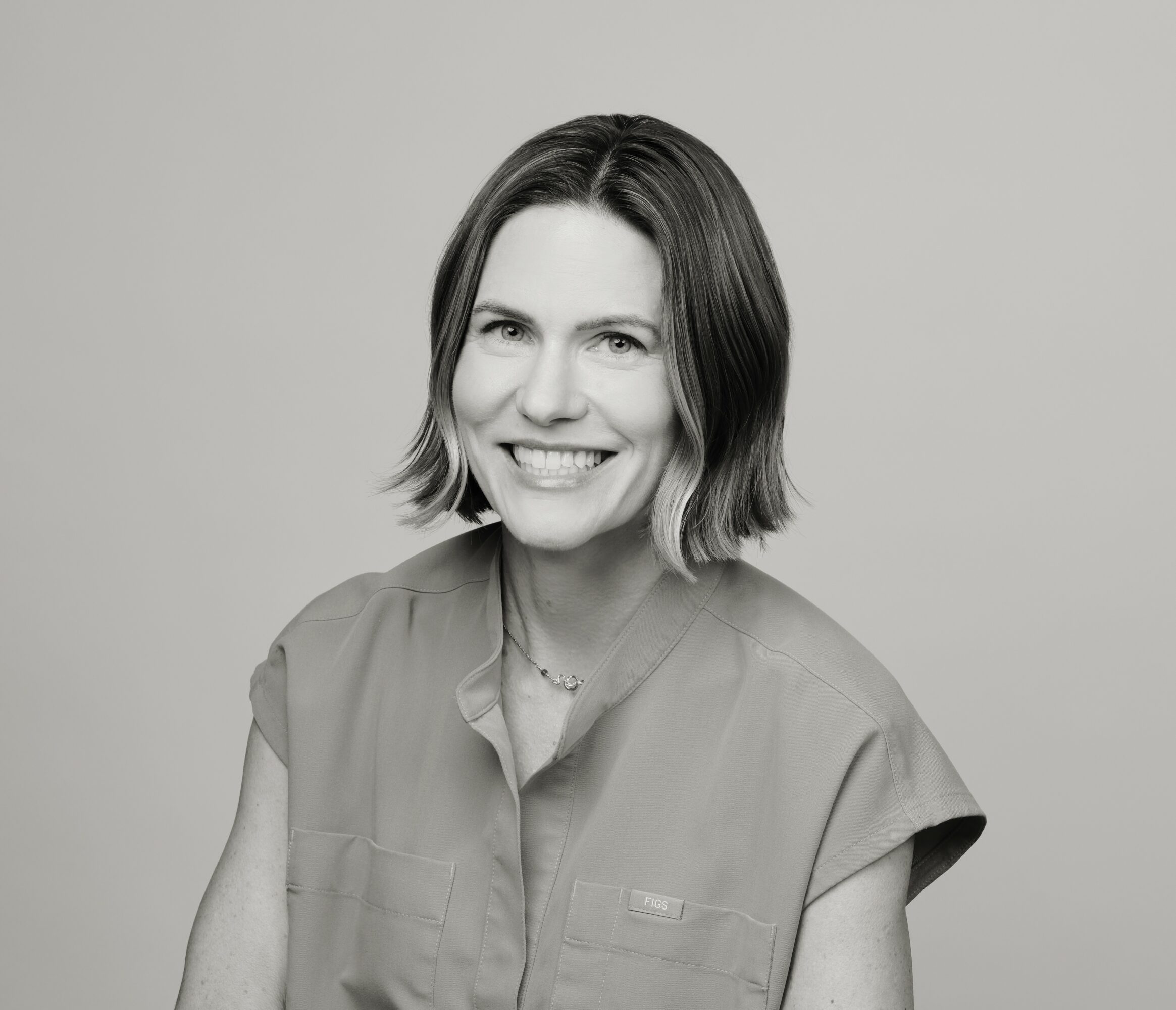 Woman with shoulder-length hair smiling, wearing a short-sleeved shirt, against a plain background.