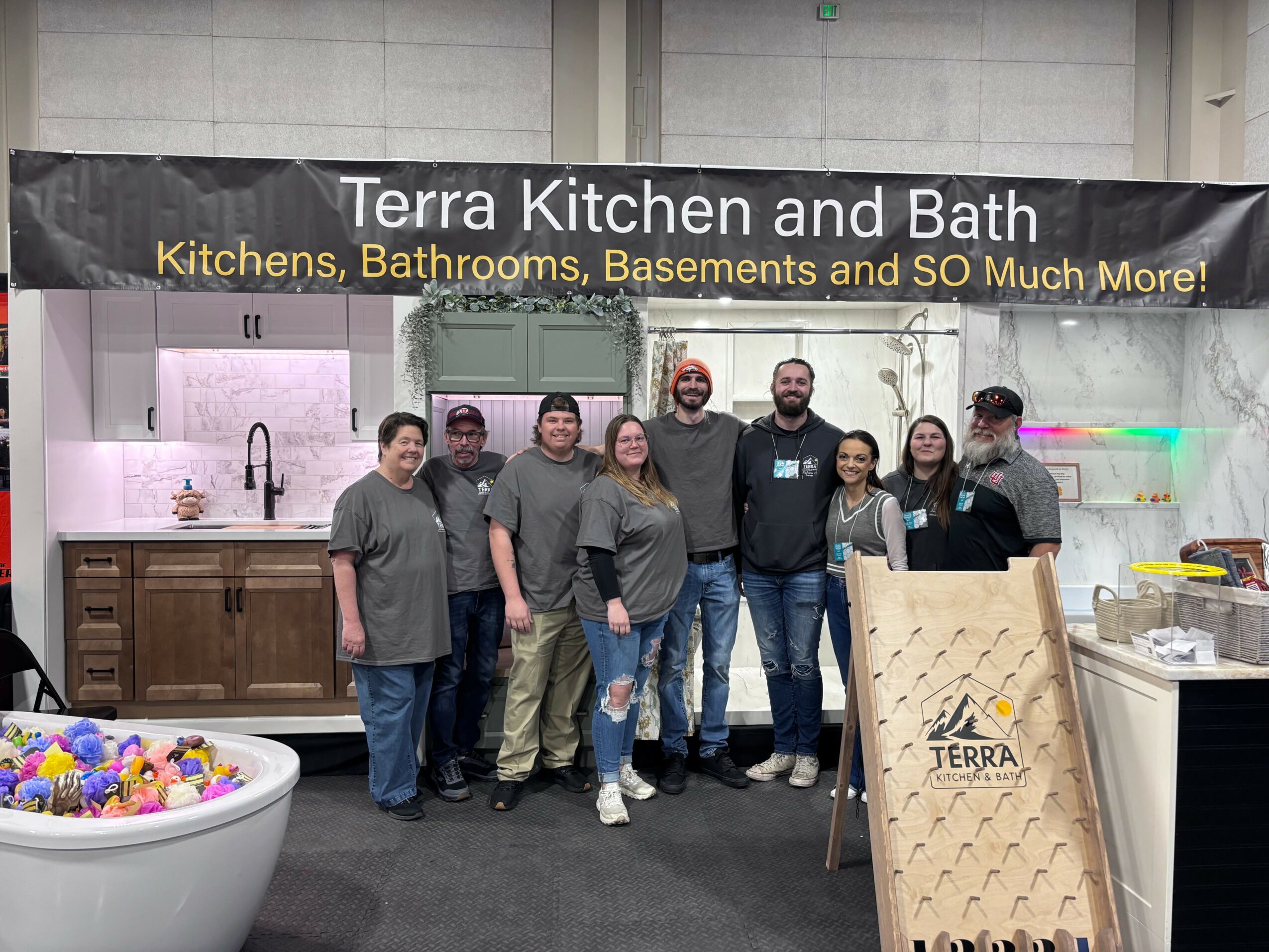 Group of seven people standing in front of a booth with a sign for Terra Kitchen and Bath, displaying kitchen and bathroom fixtures.