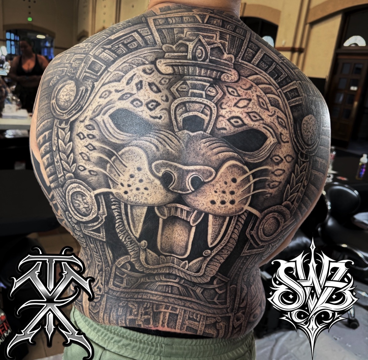Large tattoo of a jaguar's face with intricate patterns covers the person's back and shoulders.