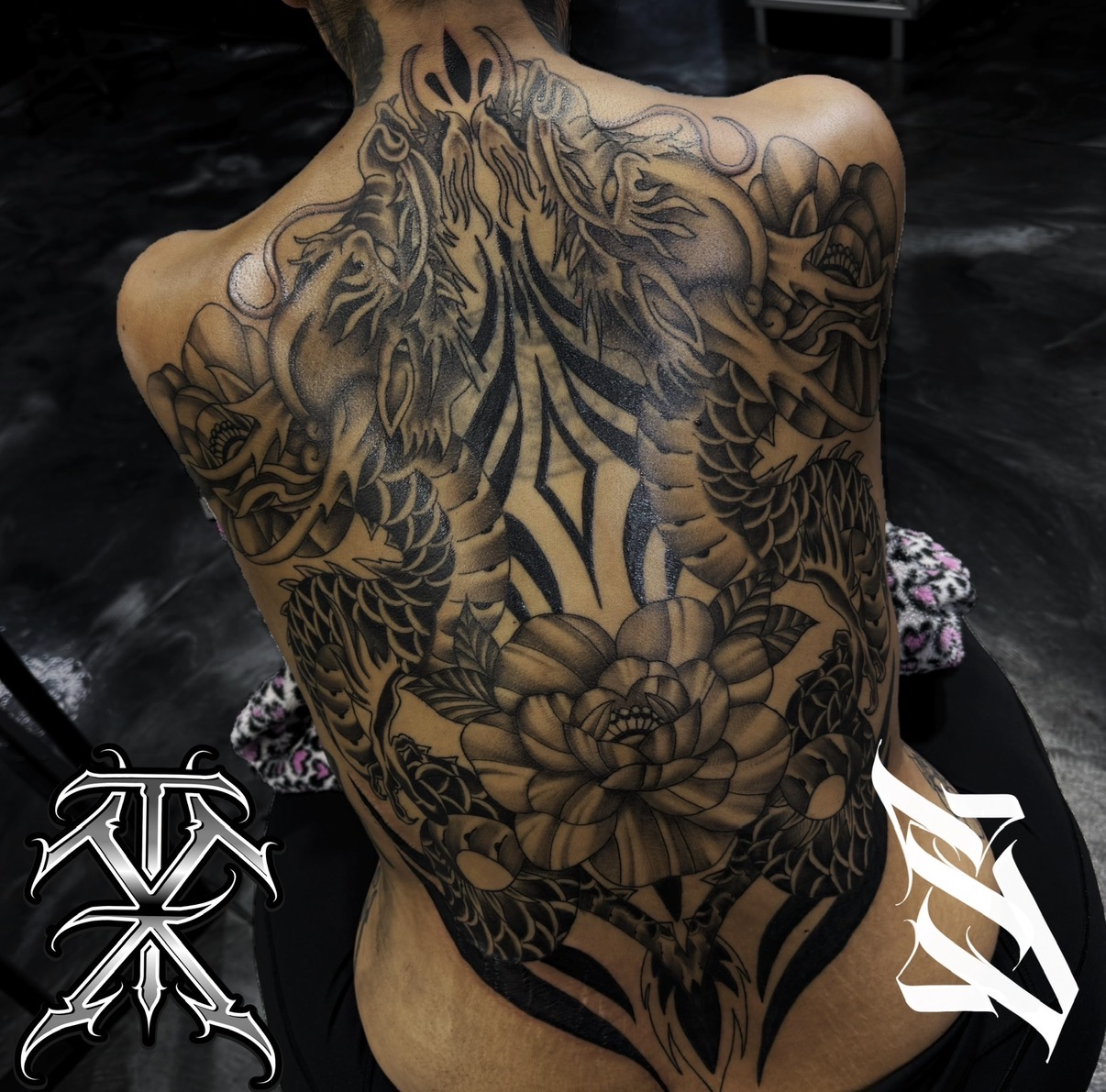 Back tattoo of a dragon with detailed scales and floral elements, covering the person's entire back.