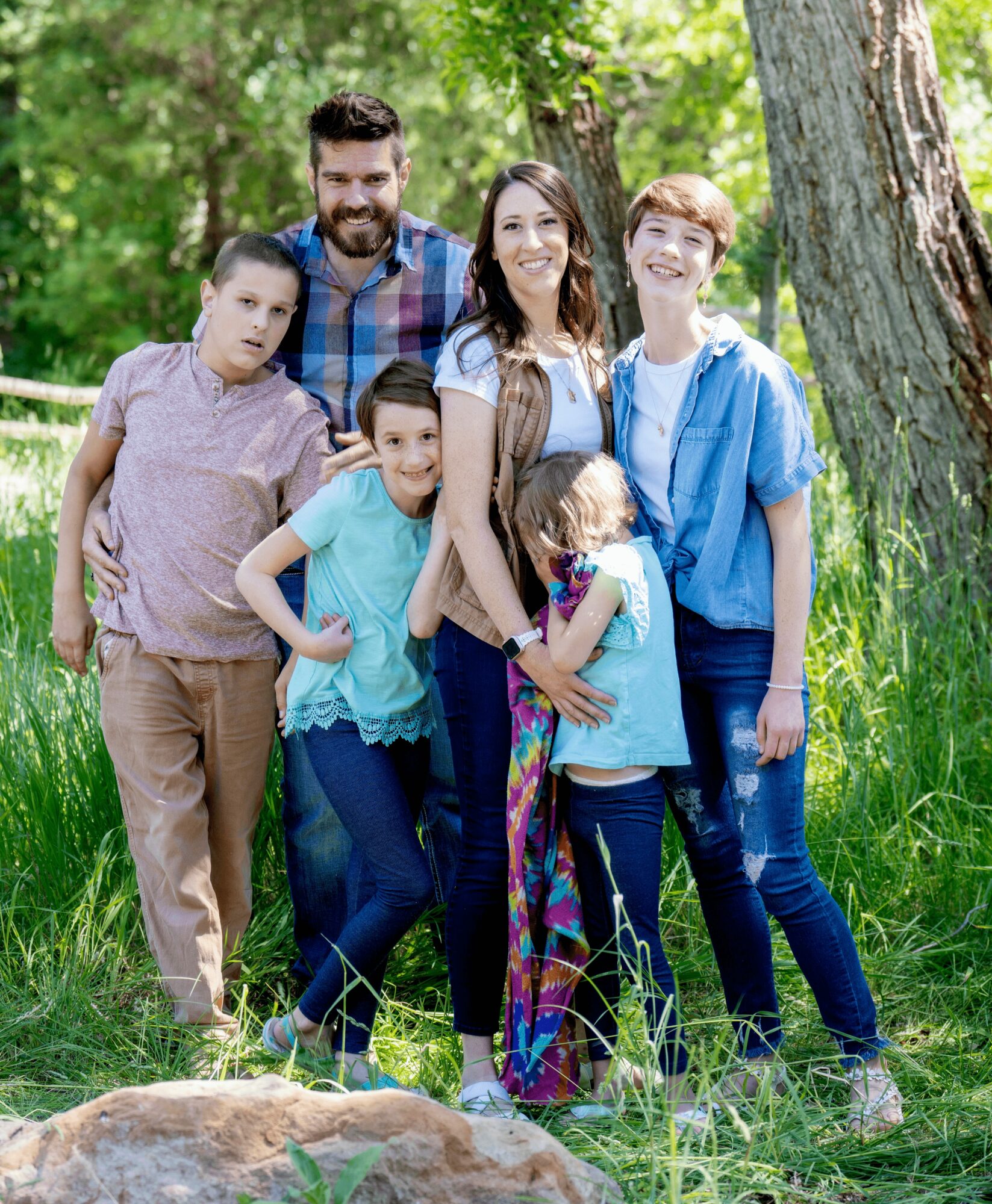 Group of six people outdoors in a grassy area with trees, smiling and posing for a photo.