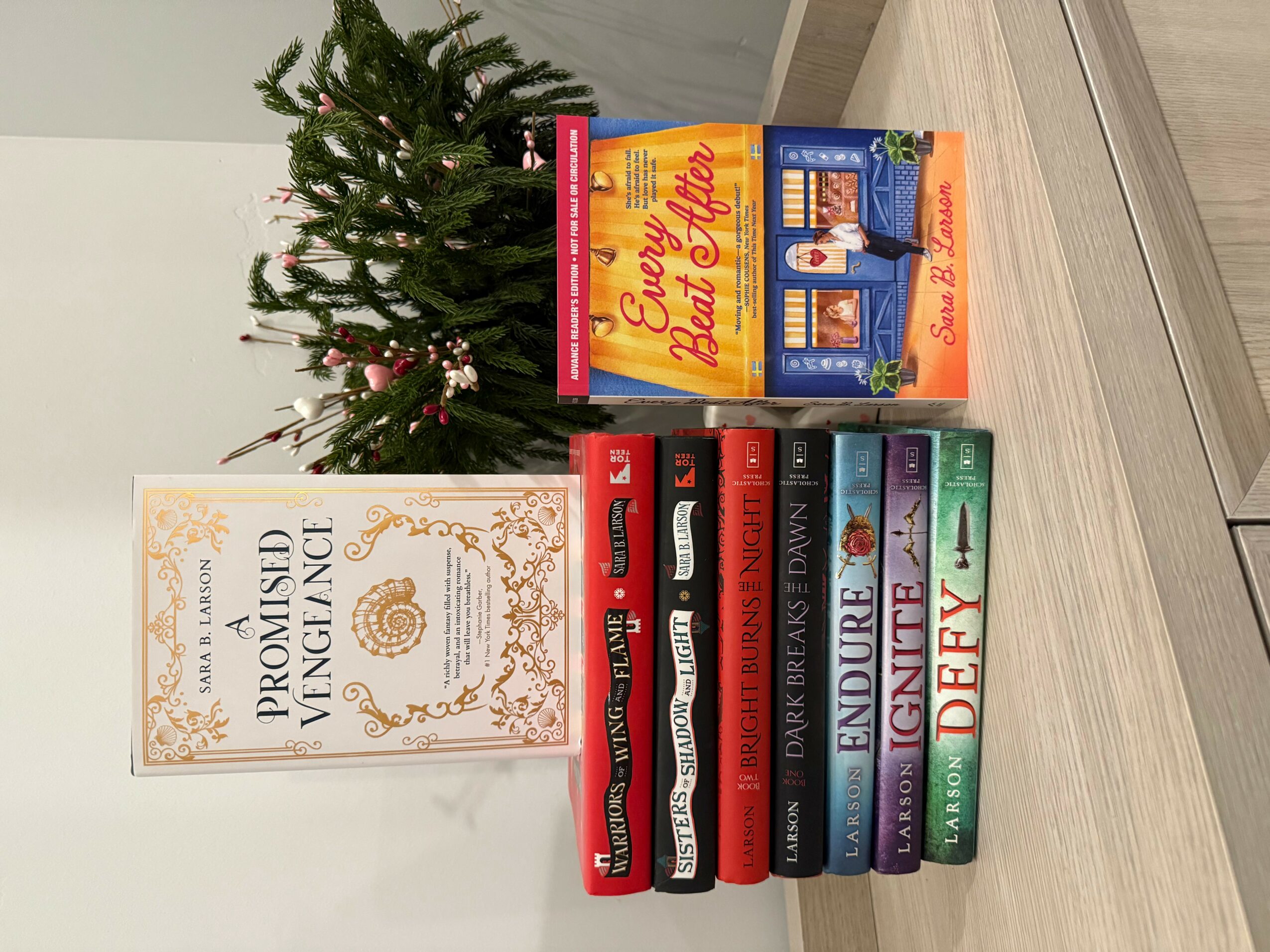 Books stacked on a table with a Christmas tree in the background, including a book titled 'The Promised Neverland' and others with colorful covers.