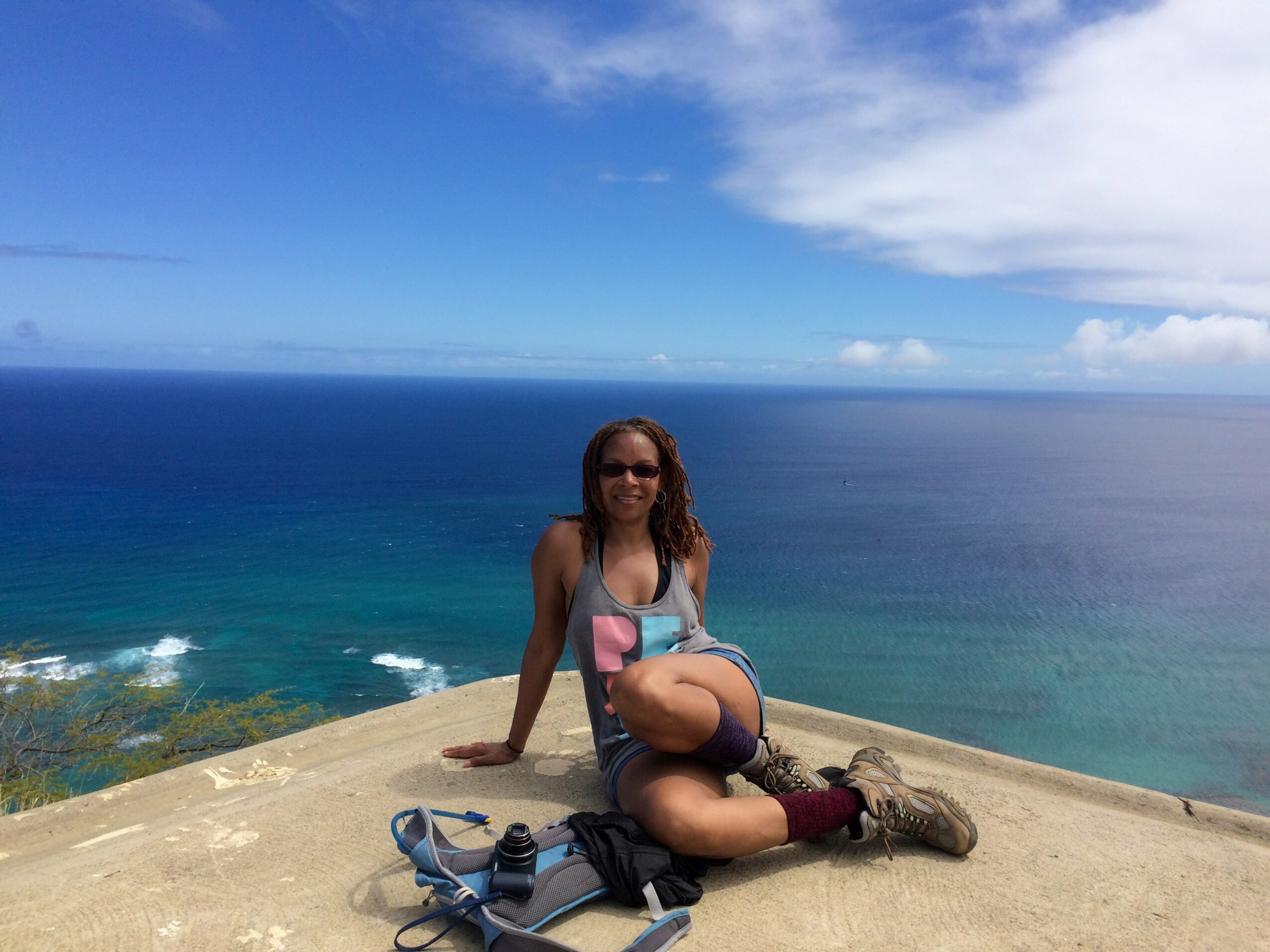 Person sitting on a ledge overlooking the ocean, with blue sky and clouds in the background.