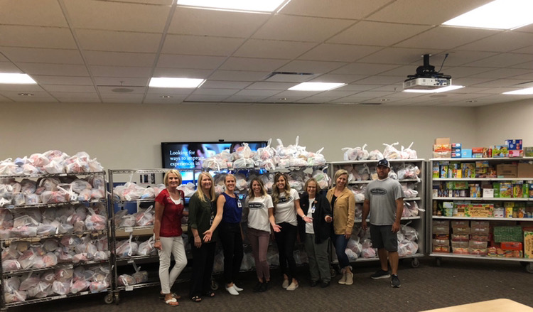Group of seven people standing in front of shelves filled with bags and boxes in a store or warehouse.