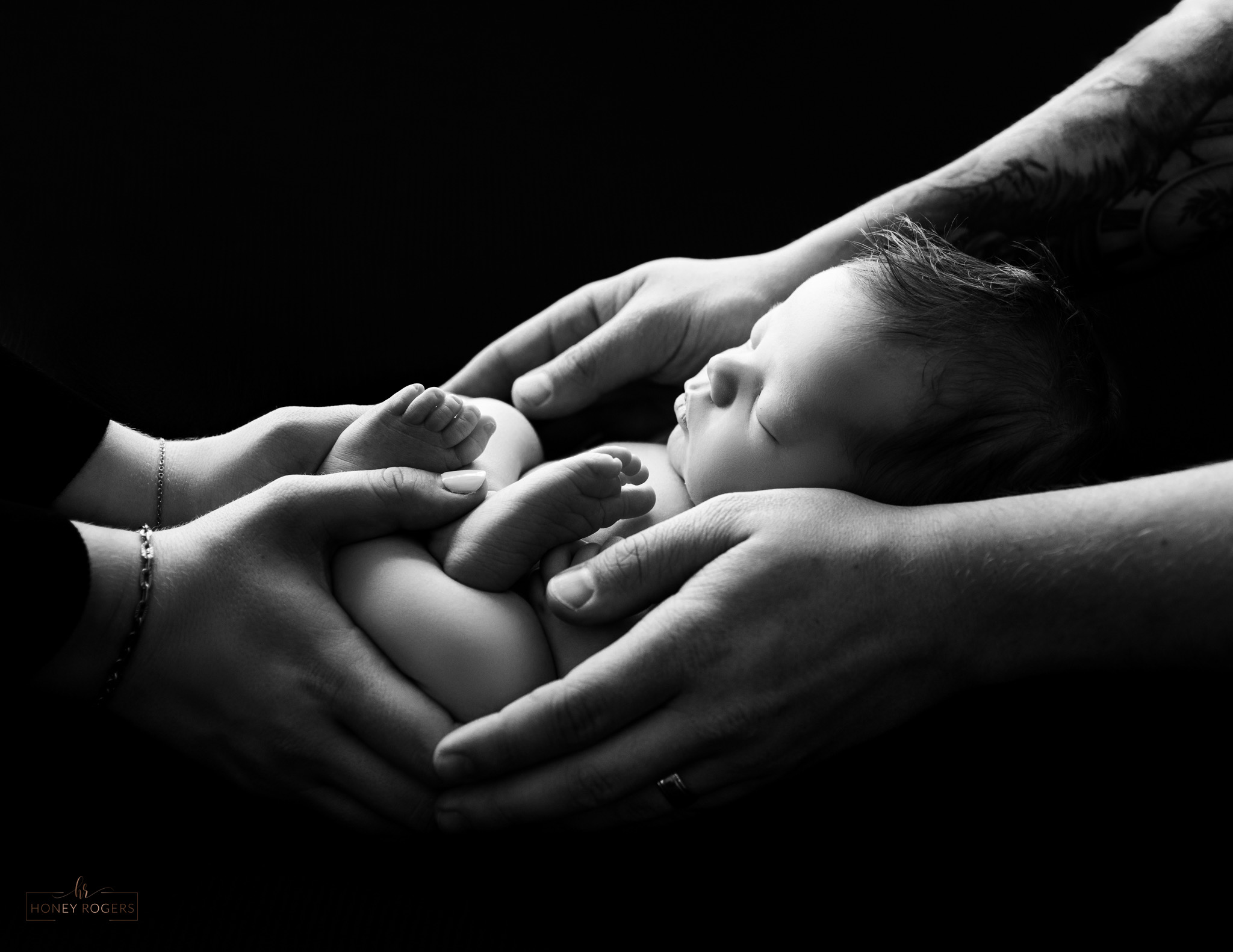 Baby sleeping in adult's hands, with adult's hands gently holding the baby, in black and white.