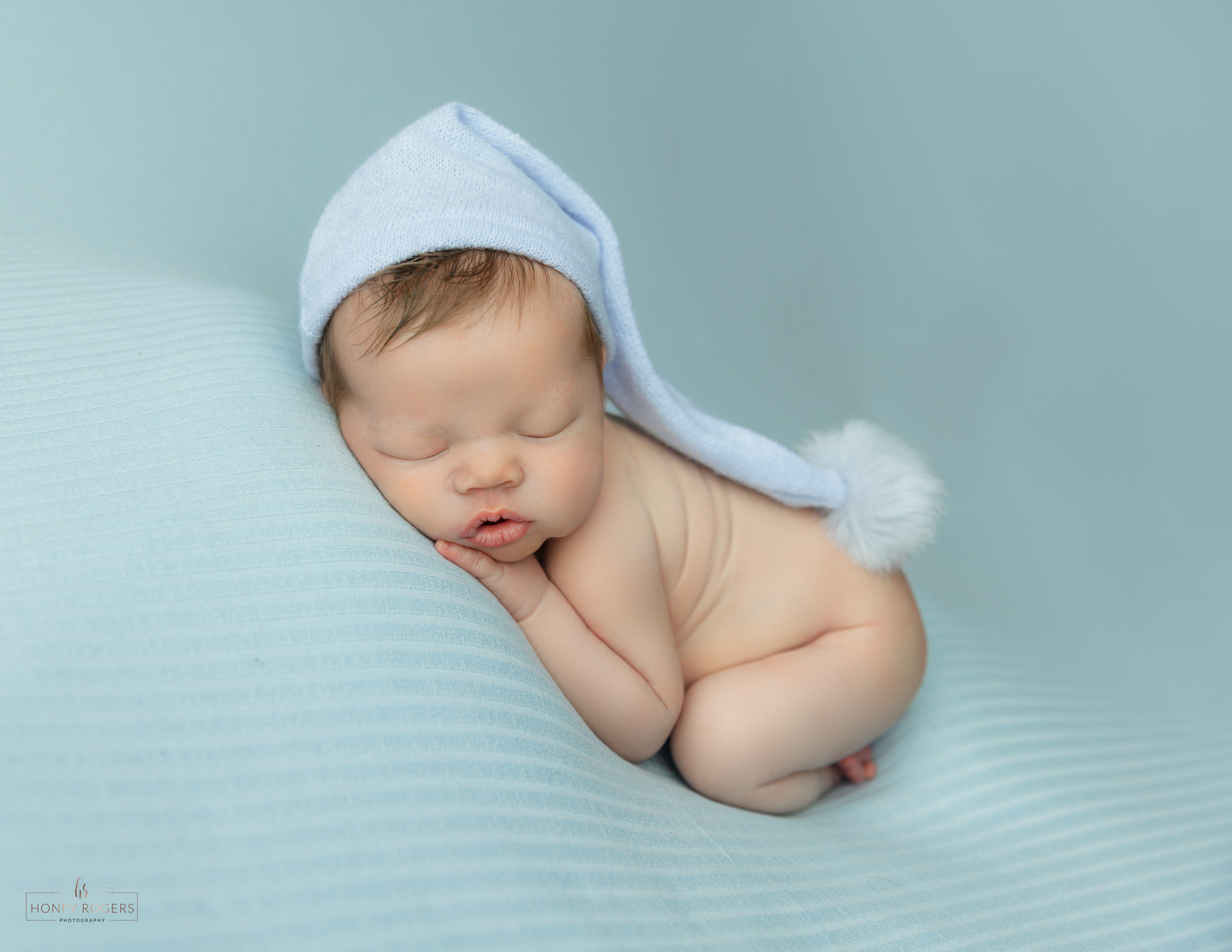 Sleeping baby with a blue hat, lying on a soft surface, resting with hands near face.