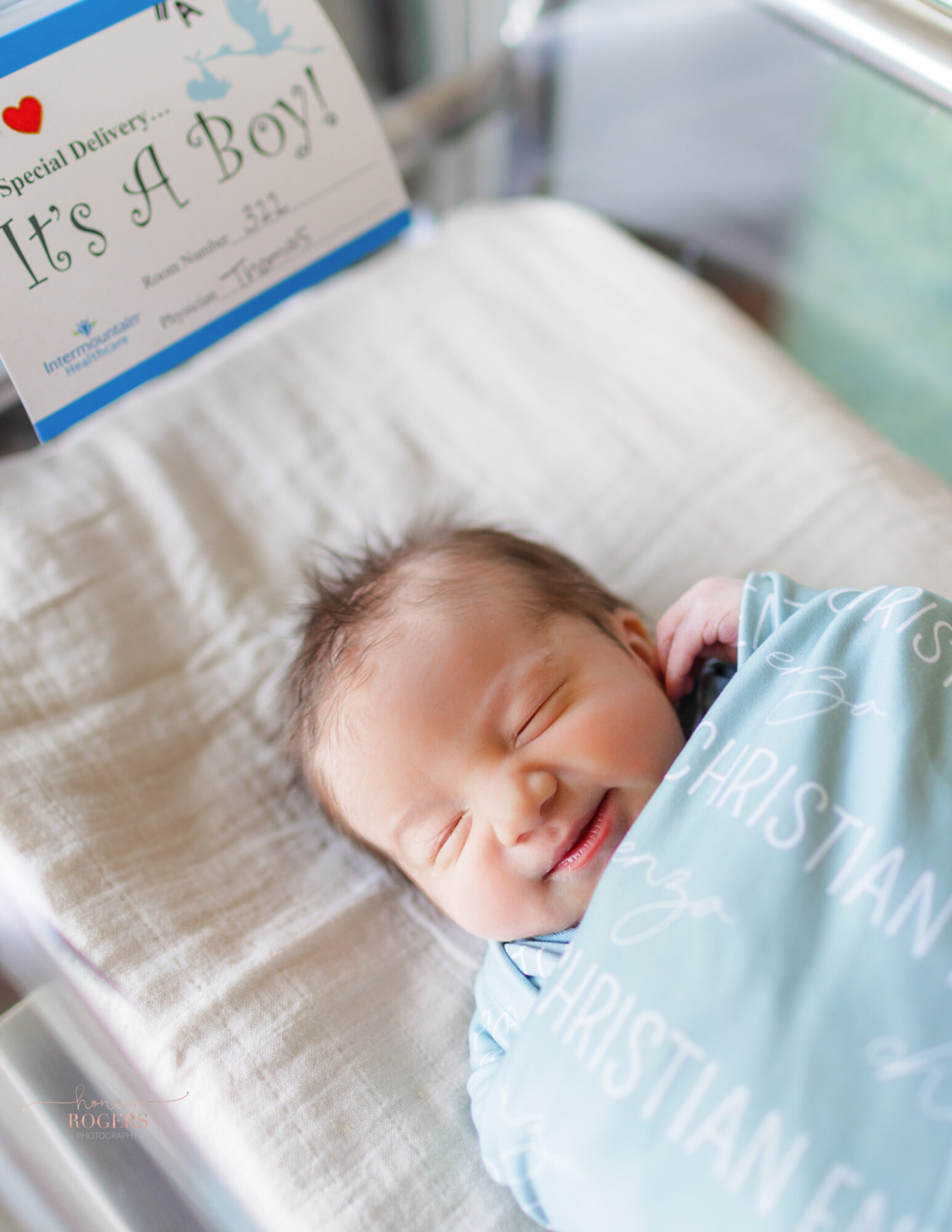 Newborn baby sleeping in a hospital bed with a sign that says 'It's A Boy!'
