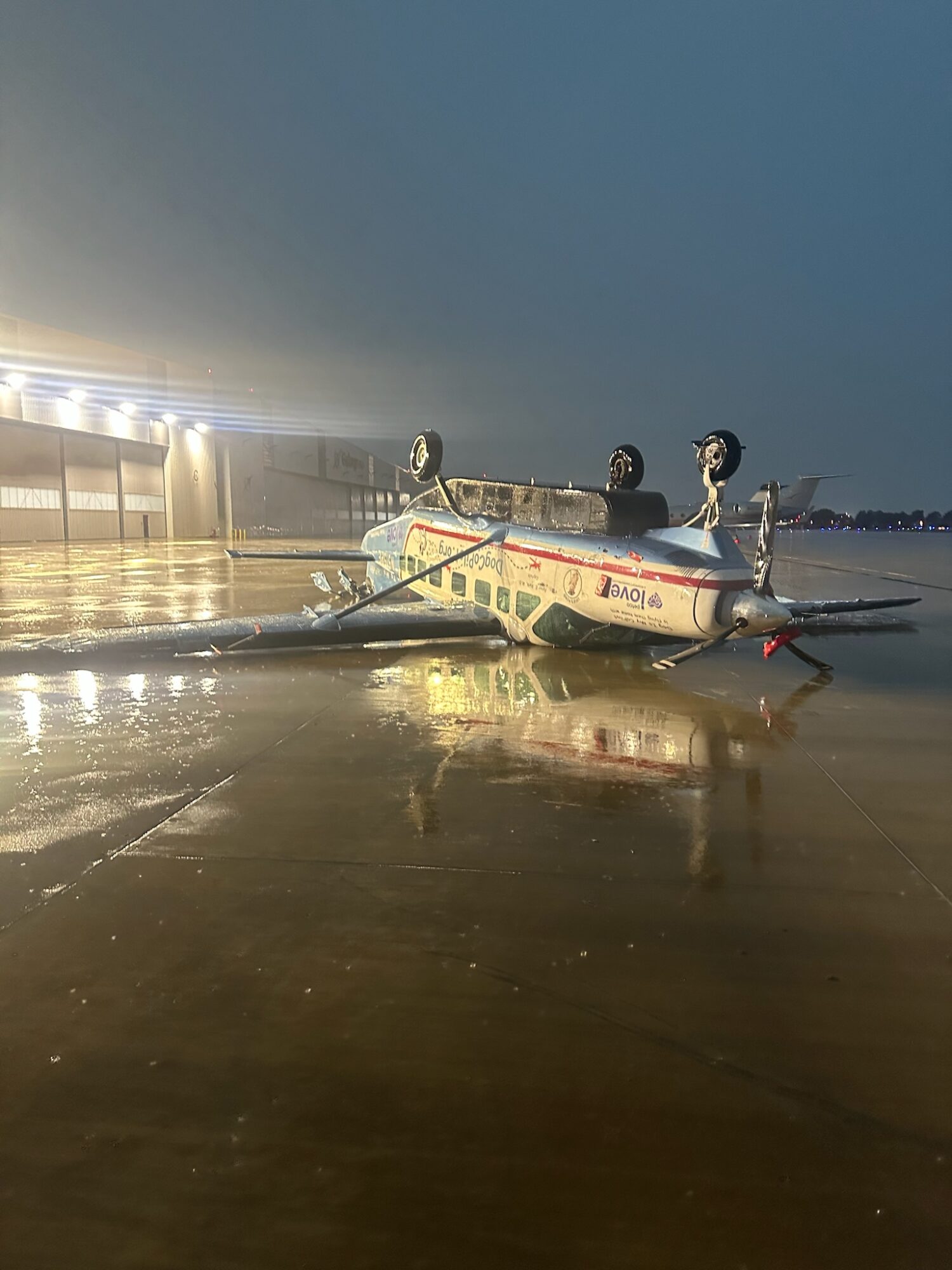 Boat overturned on wet sand near a pier, with water and sky in the background, illuminated by lights, reflecting on the surface.