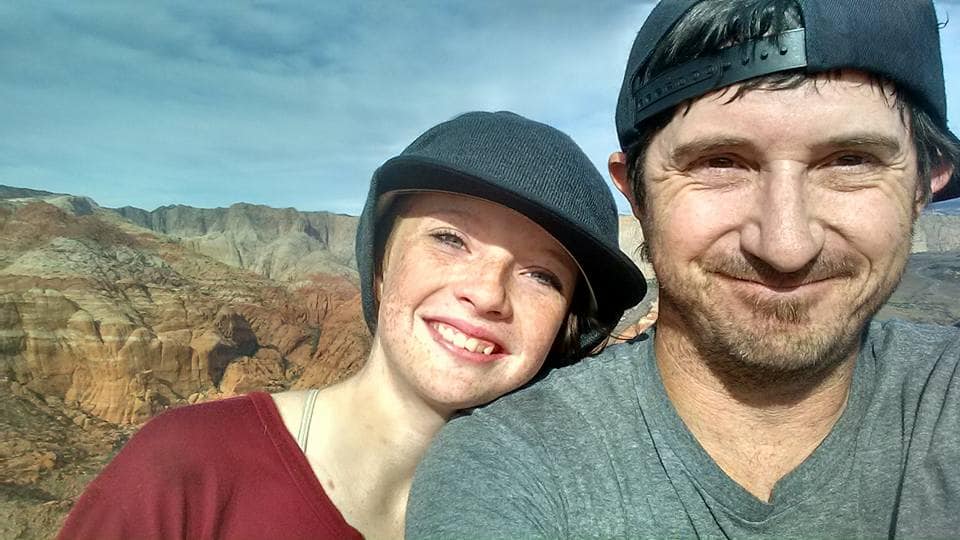 Two people smiling outdoors with a mountainous landscape in the background.