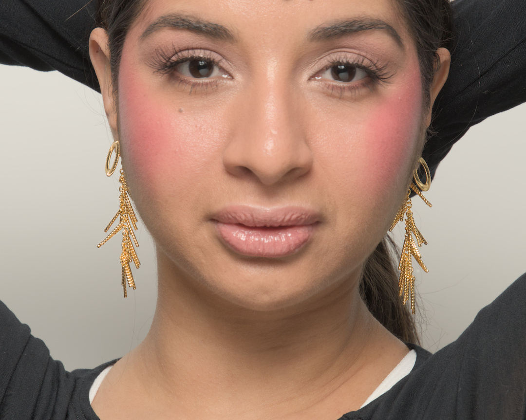 Close-up of a woman with makeup, earrings, and dark hair, looking directly at the camera.