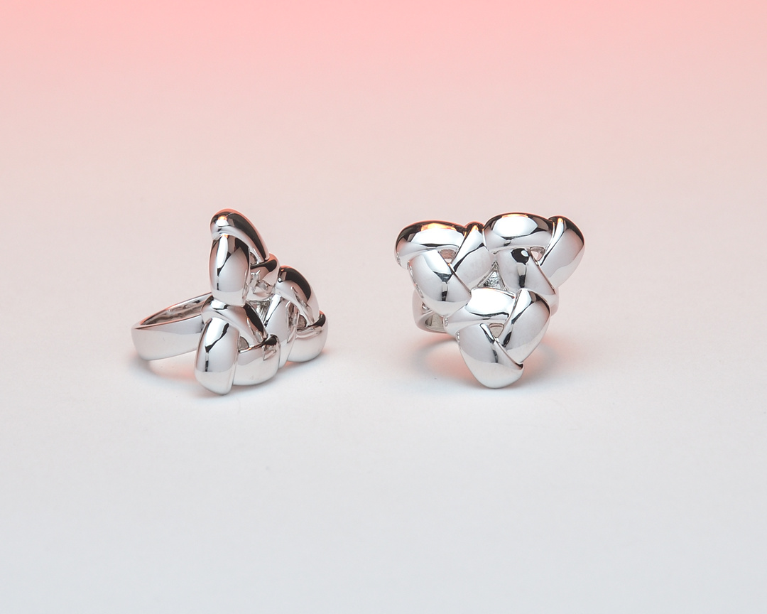 Two shiny metallic abstract sculptures on a pink and white gradient background.