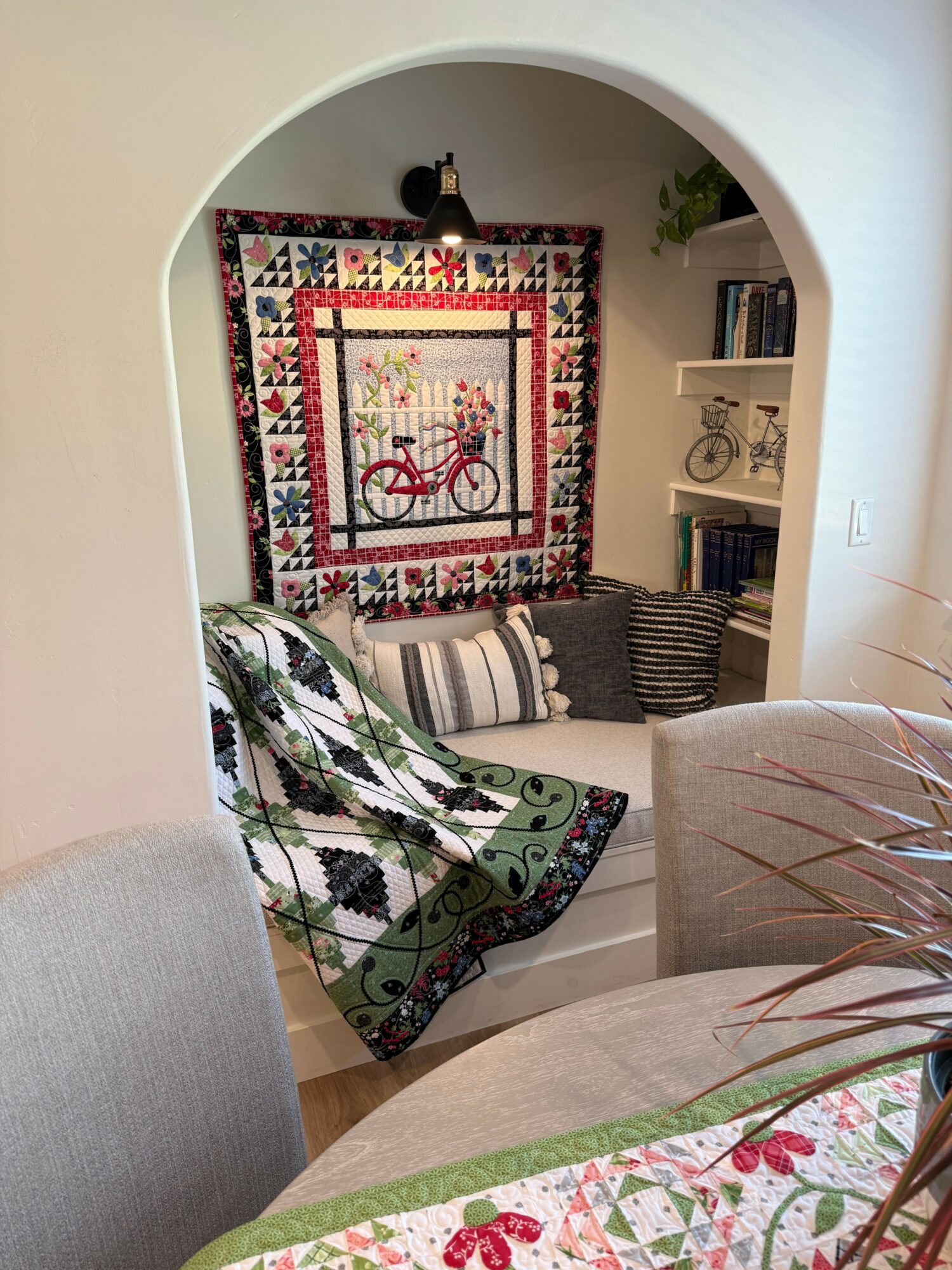 Living room with a colorful quilt hanging on the wall, a patterned rug, and a striped pillow on a chair.