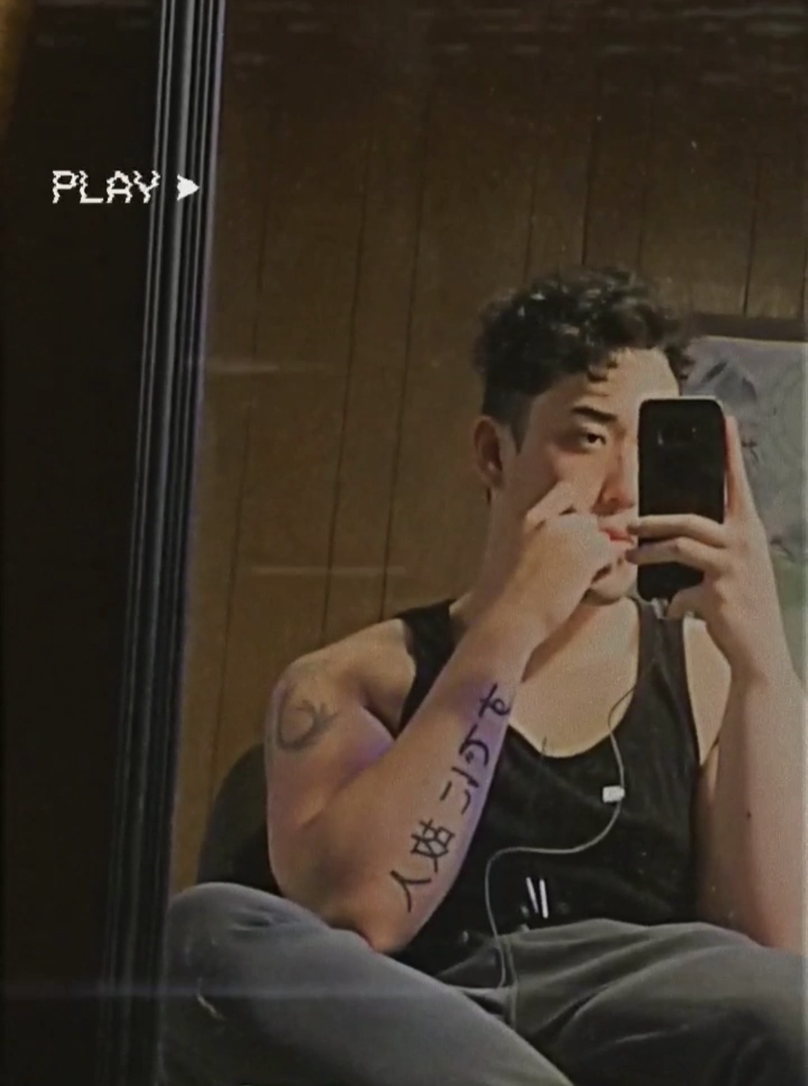 Person taking a mirror selfie with a smartphone, sitting indoors with wooden wall background.