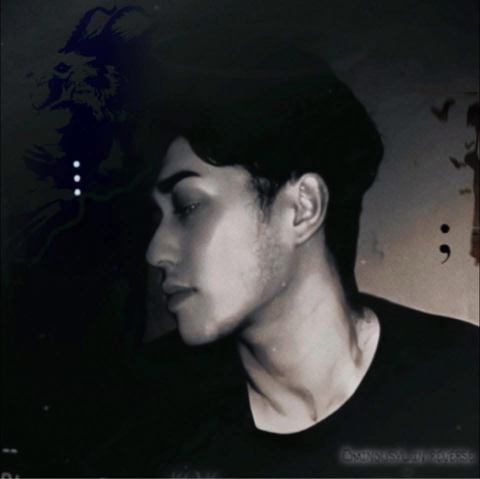 Side profile of a young person with short dark hair, looking downward, in a dark setting.