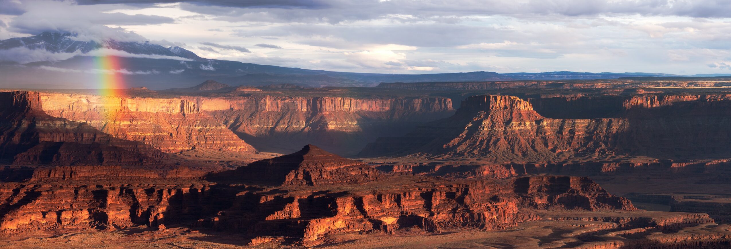 Grand canyon landscape with cliffs and a rainbow in the sky.