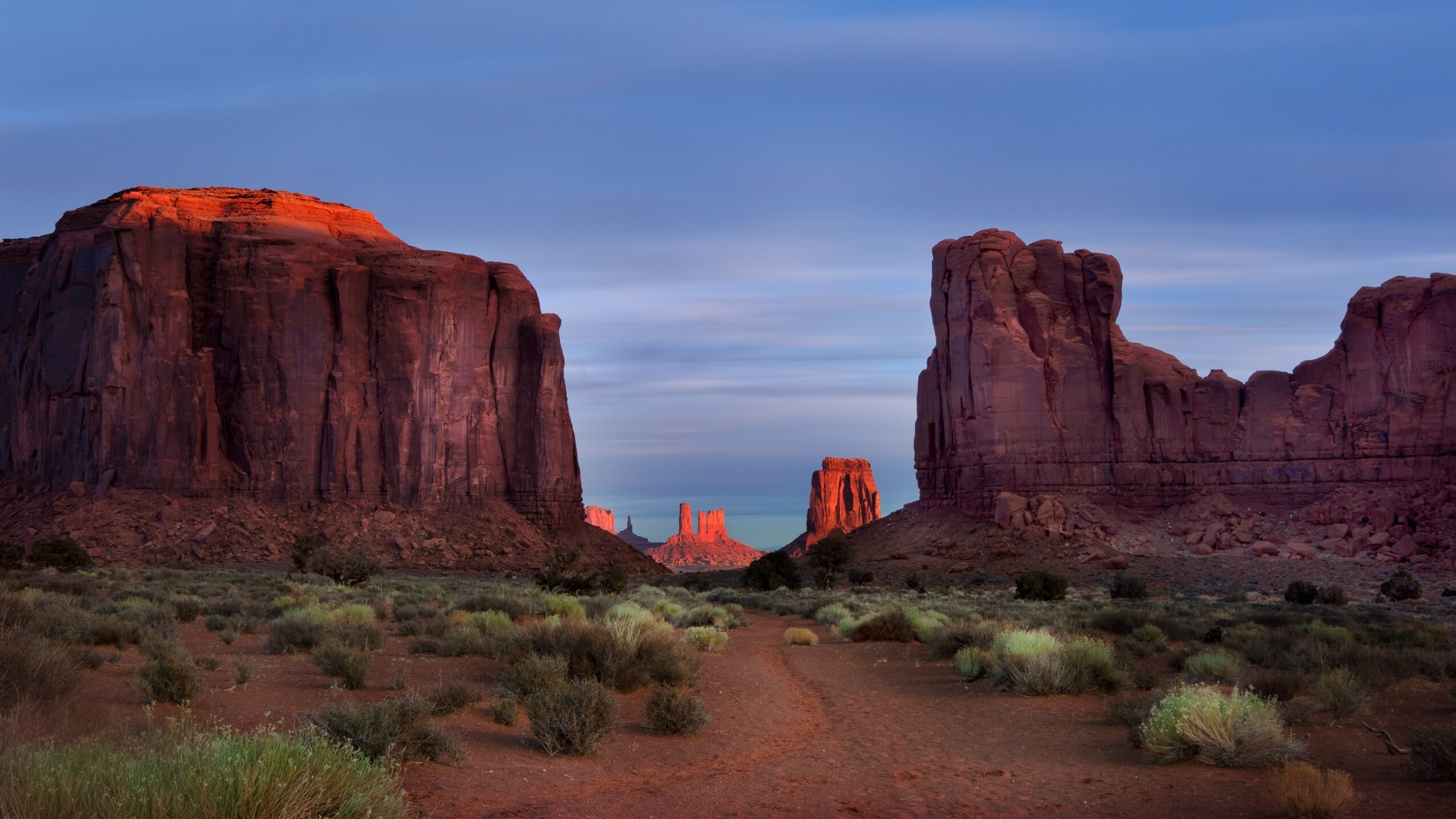 Desert landscape with large rock formations and sparse vegetation under a cloudy sky.