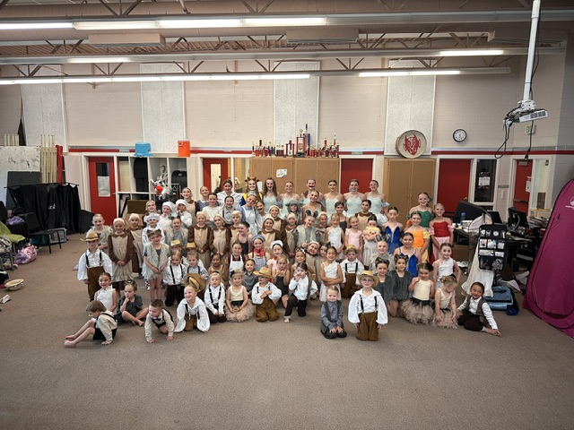 Group of children and adults in a classroom or studio, posing for a photo, with colorful cabinets and equipment in the background.