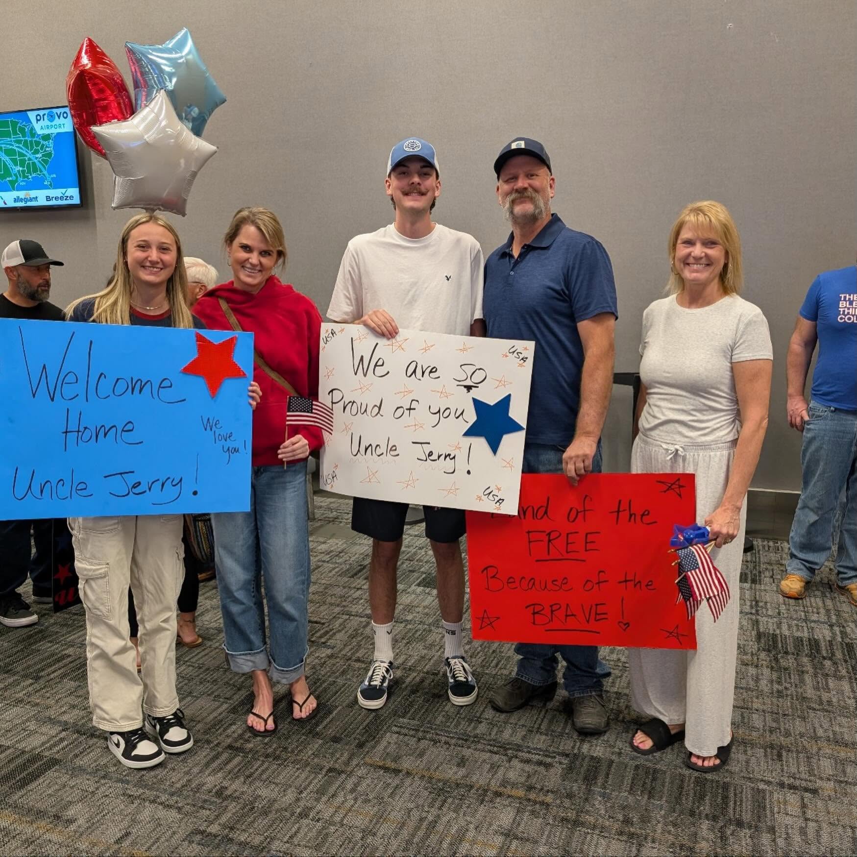 Group of five people holding signs, celebrating Uncle Jerry's return, with balloons in background.
