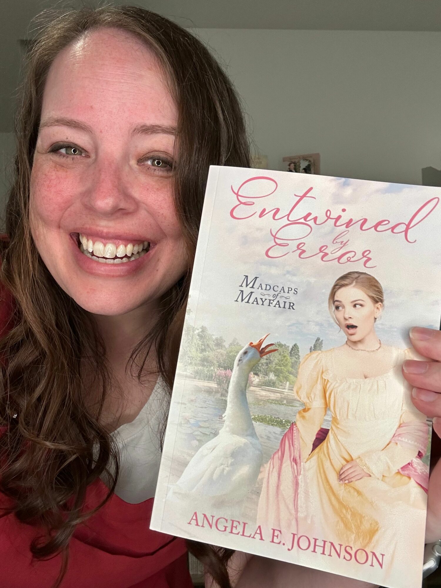 Woman smiling holding a book titled 'Entwined in Love' with a woman in a yellow dress on the cover.
