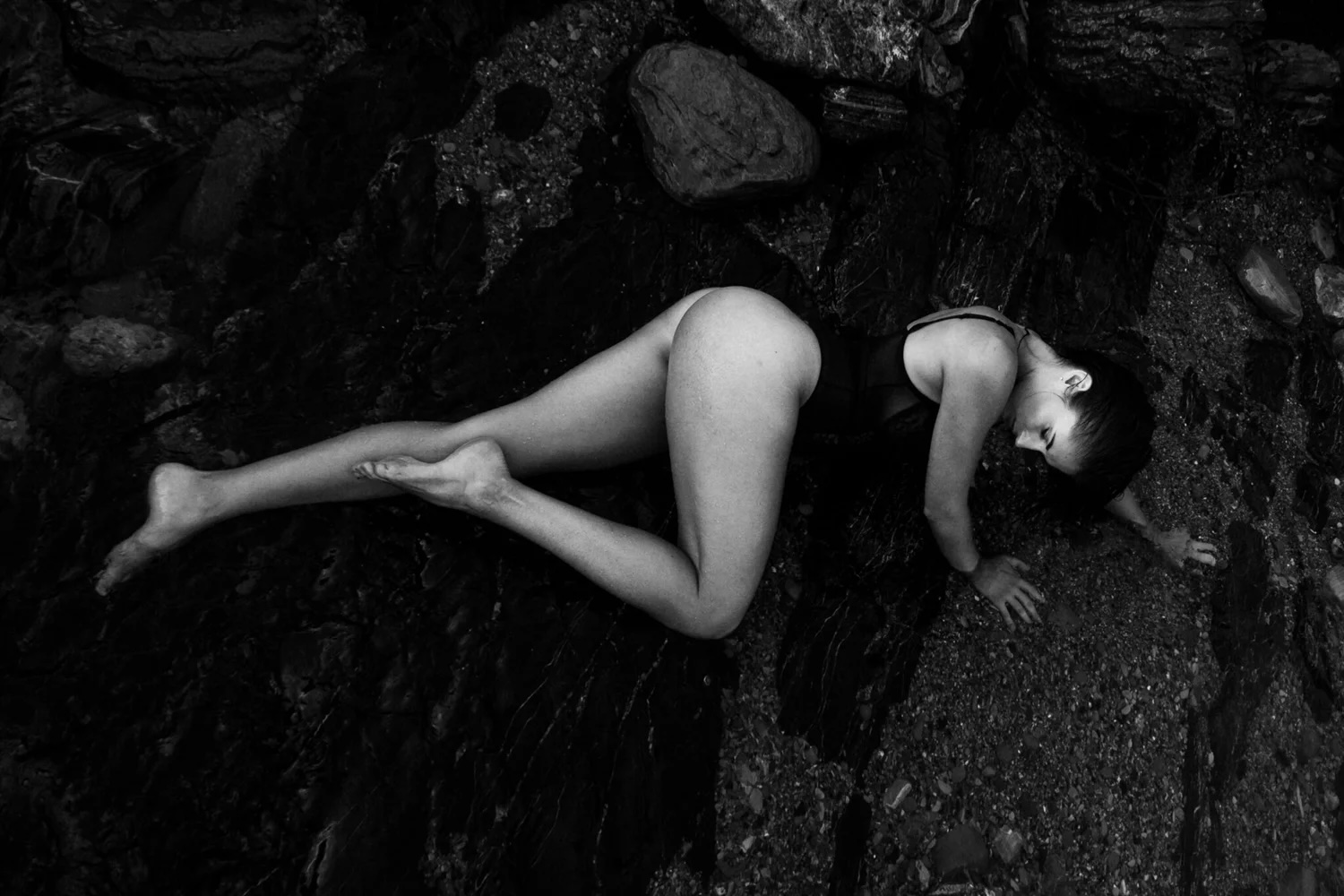 Person lying on rocks with head turned to the side, body curved, in black and white.