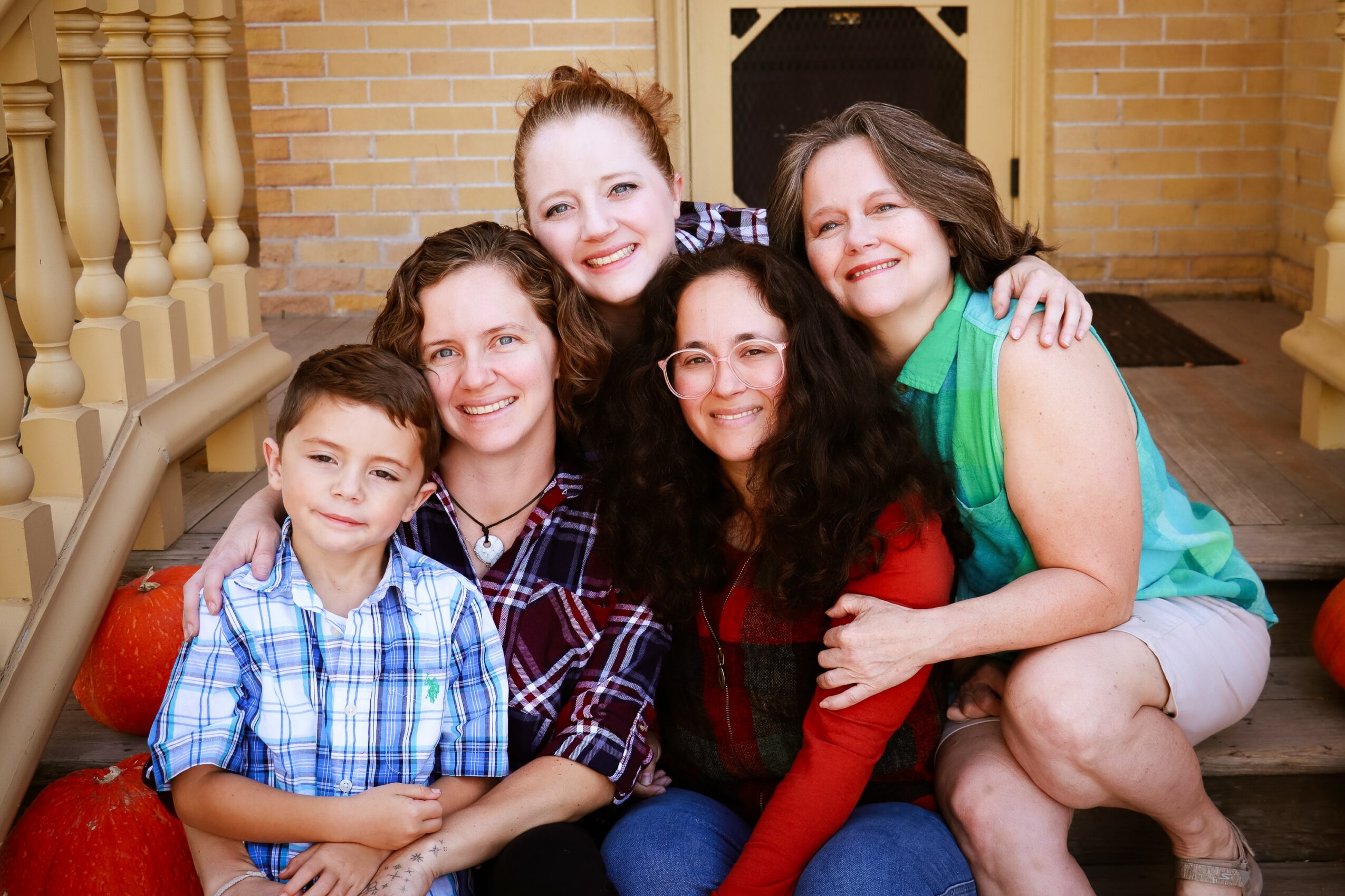 Group of five people, including children and adults, smiling and sitting together on steps outside a brick building.