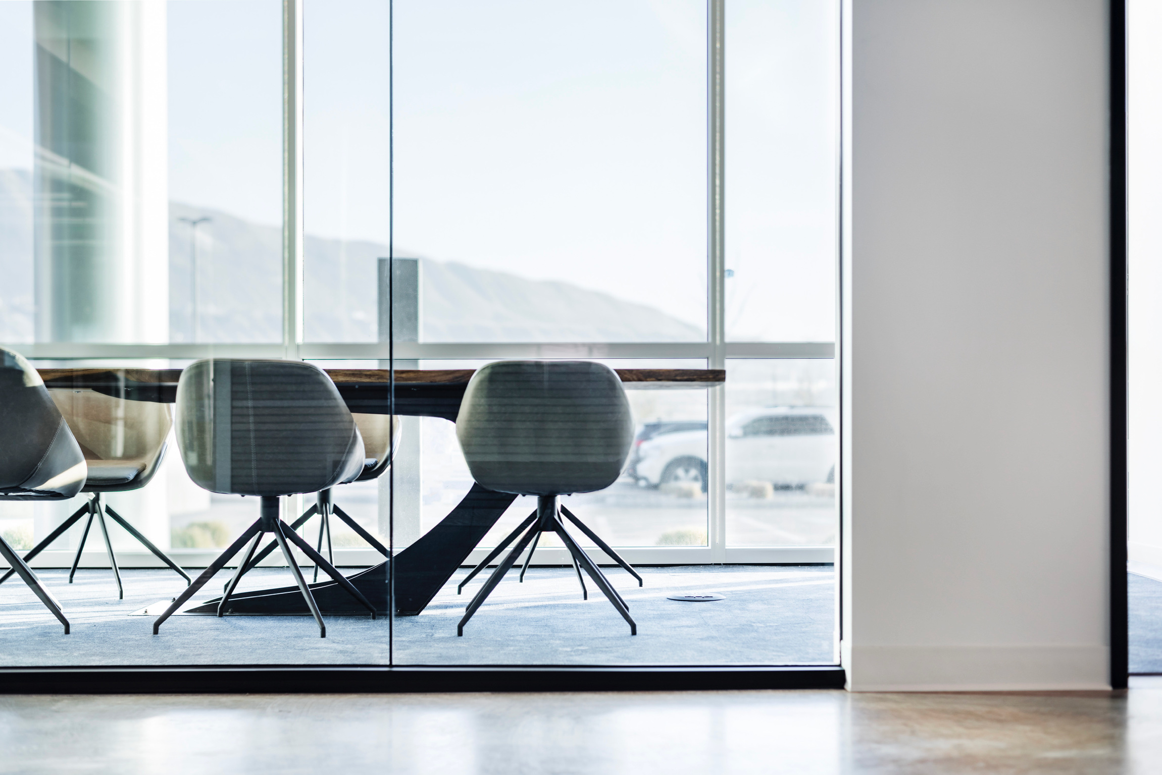 Three chairs are positioned in front of a large glass window in a modern room, with a view outside.