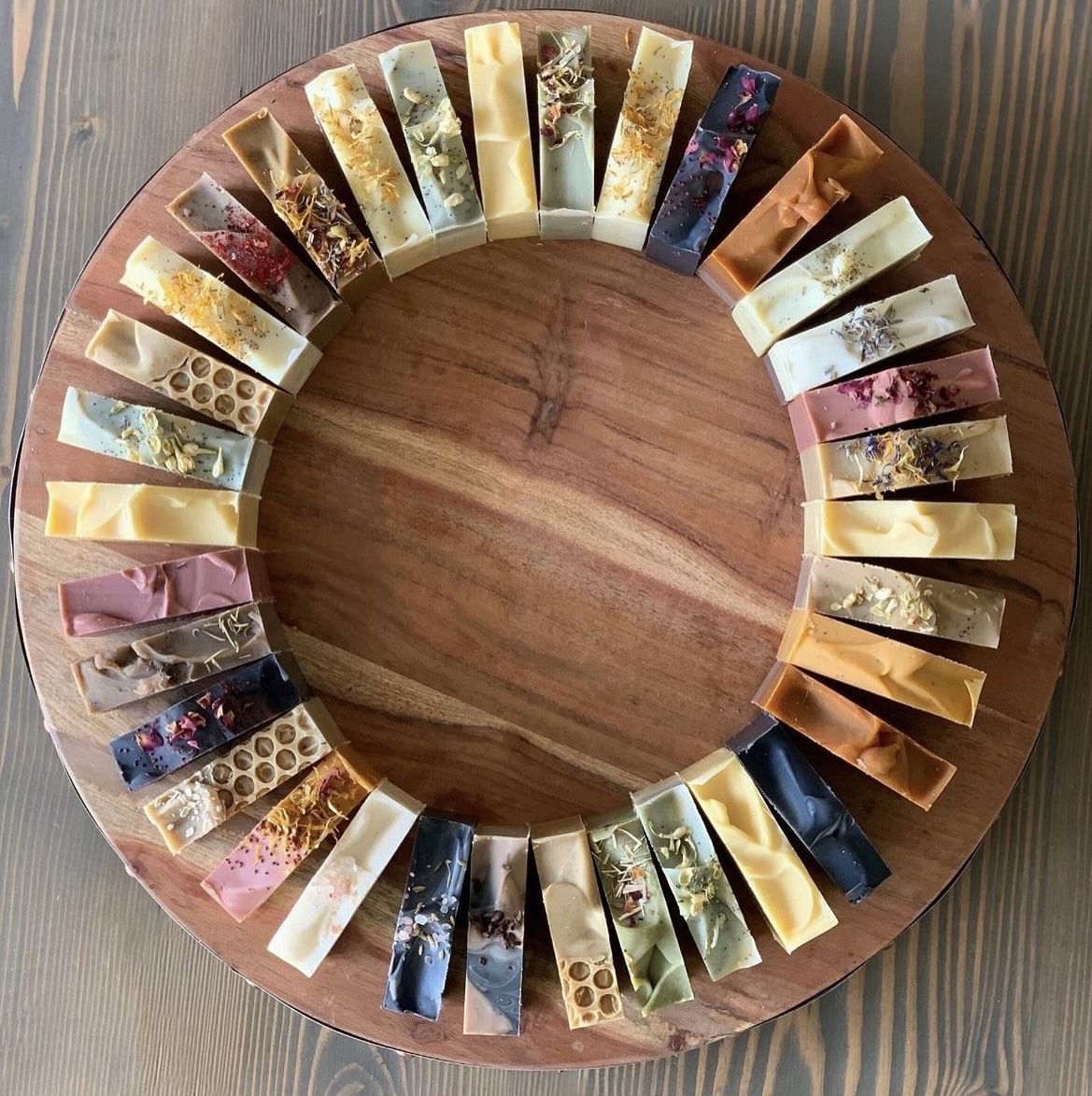A circular wooden tray with various soap bars arranged around the edge, each with different colors and patterns.