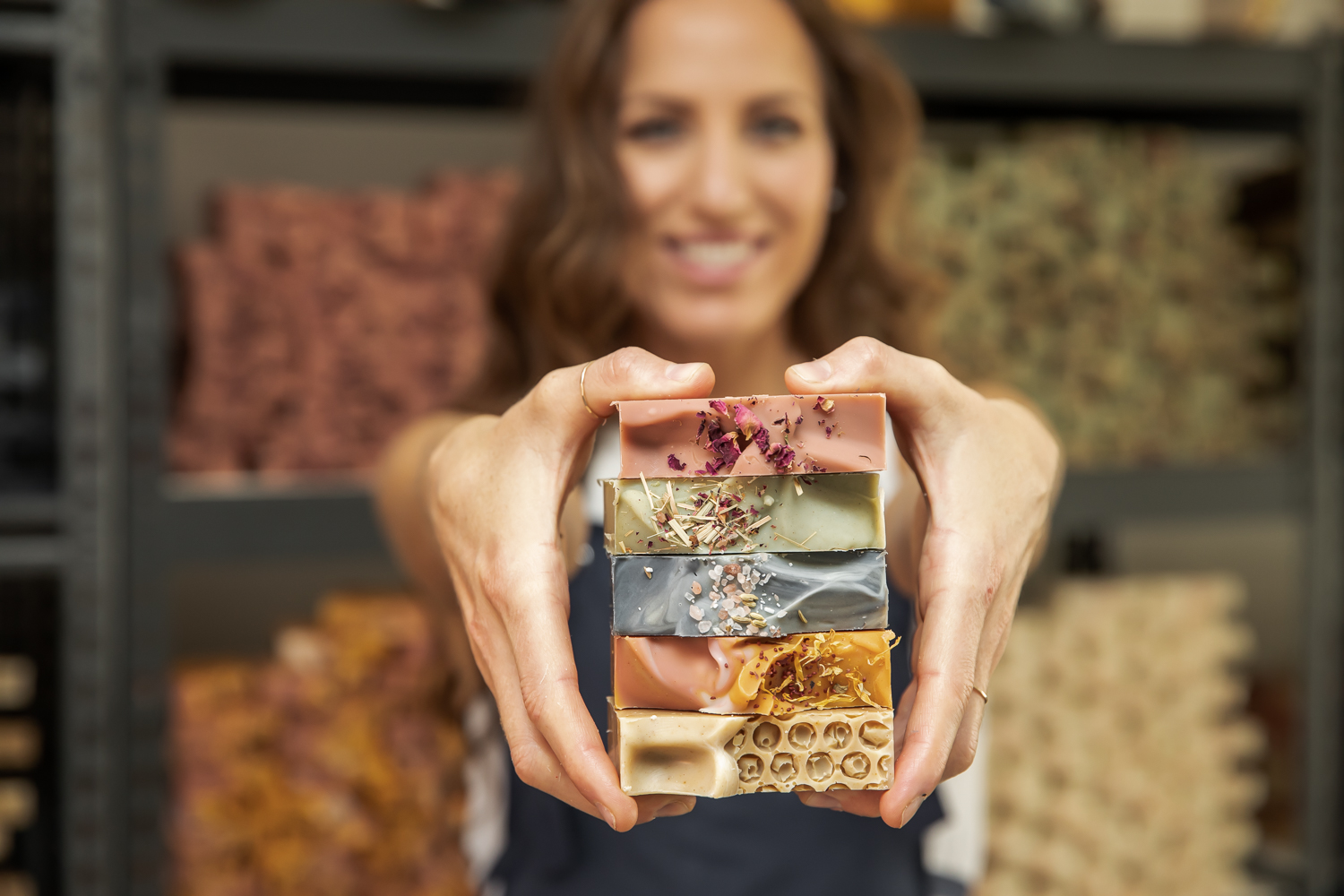 Person holding a stack of soap bars with blurred background of shelves and colorful fabrics.