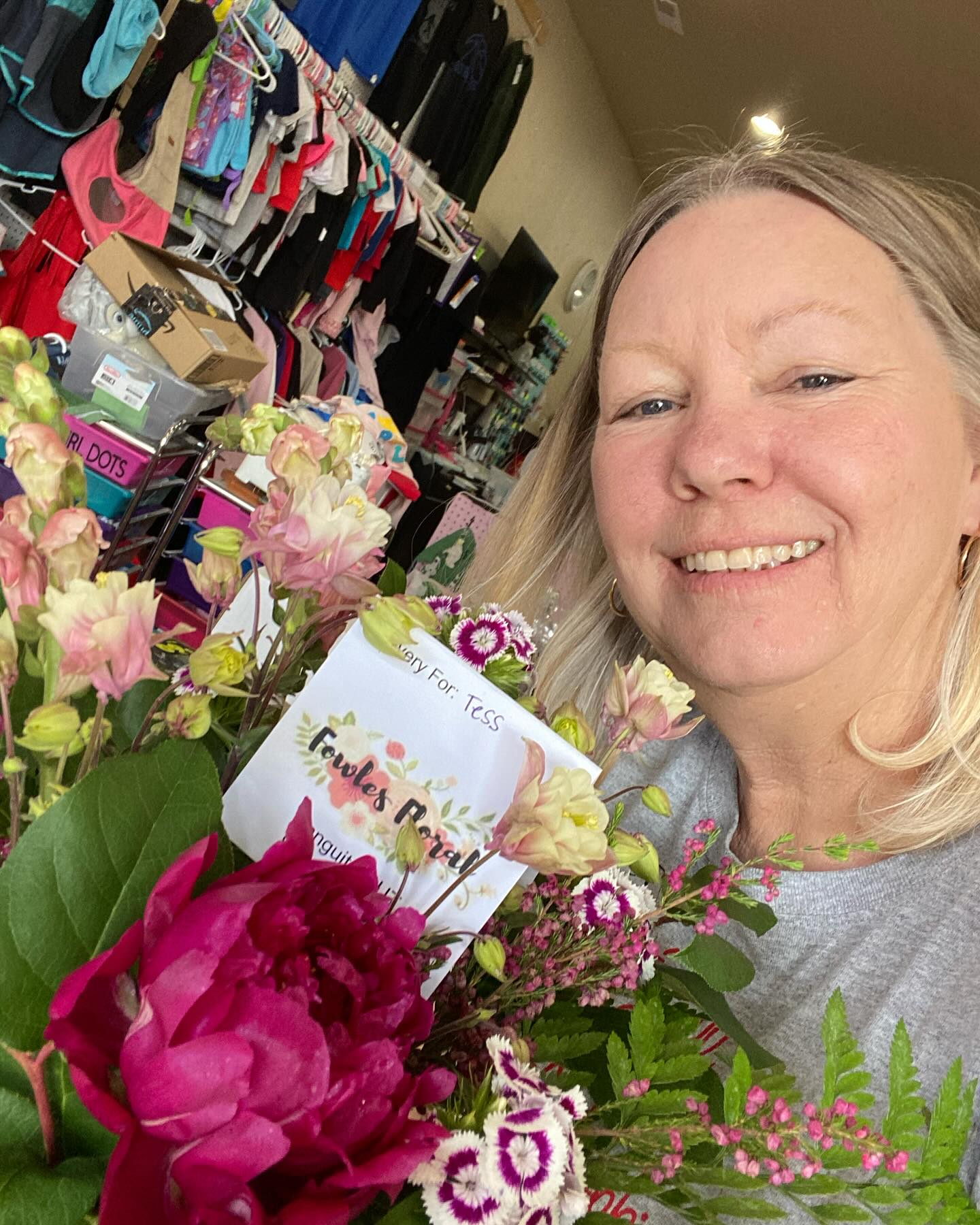 Woman smiling with flowers in a store, clothing racks in background.