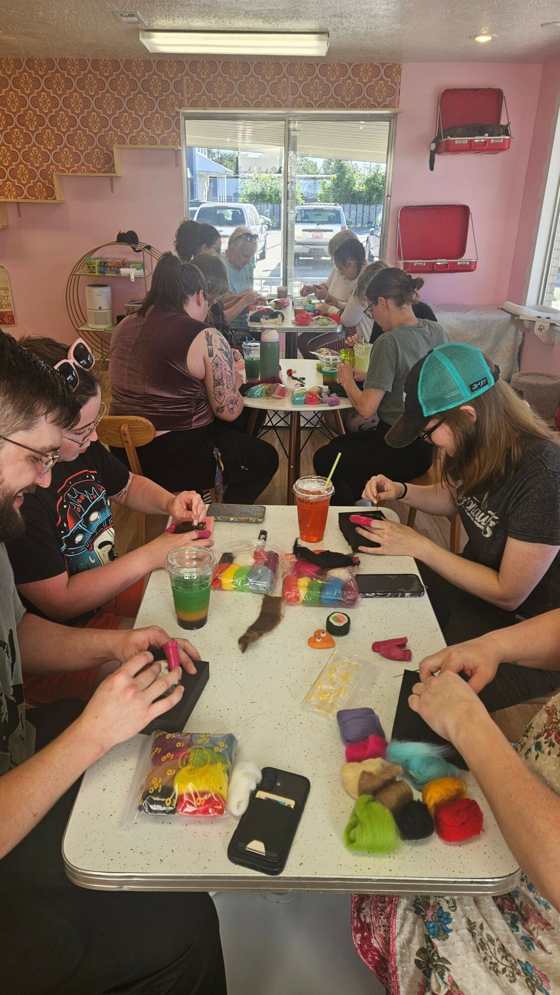 People gathered around a table with colorful craft supplies, working on a creative project in a bright room.