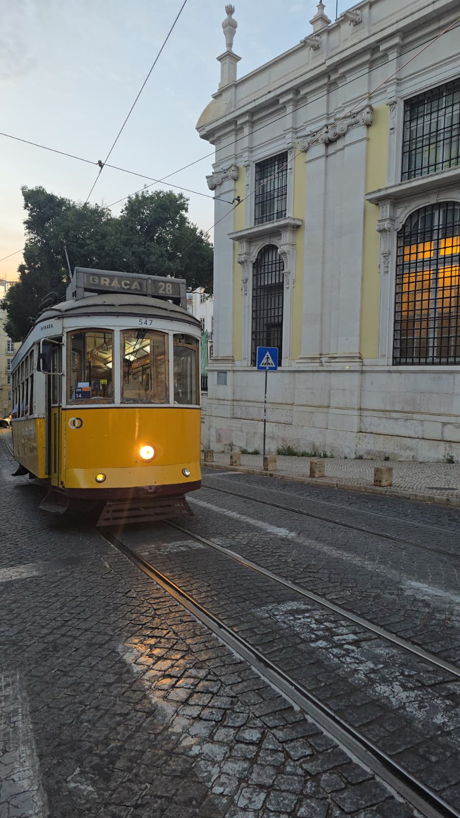 Yellow tram on cobblestone street next to a historic white building with barred windows.