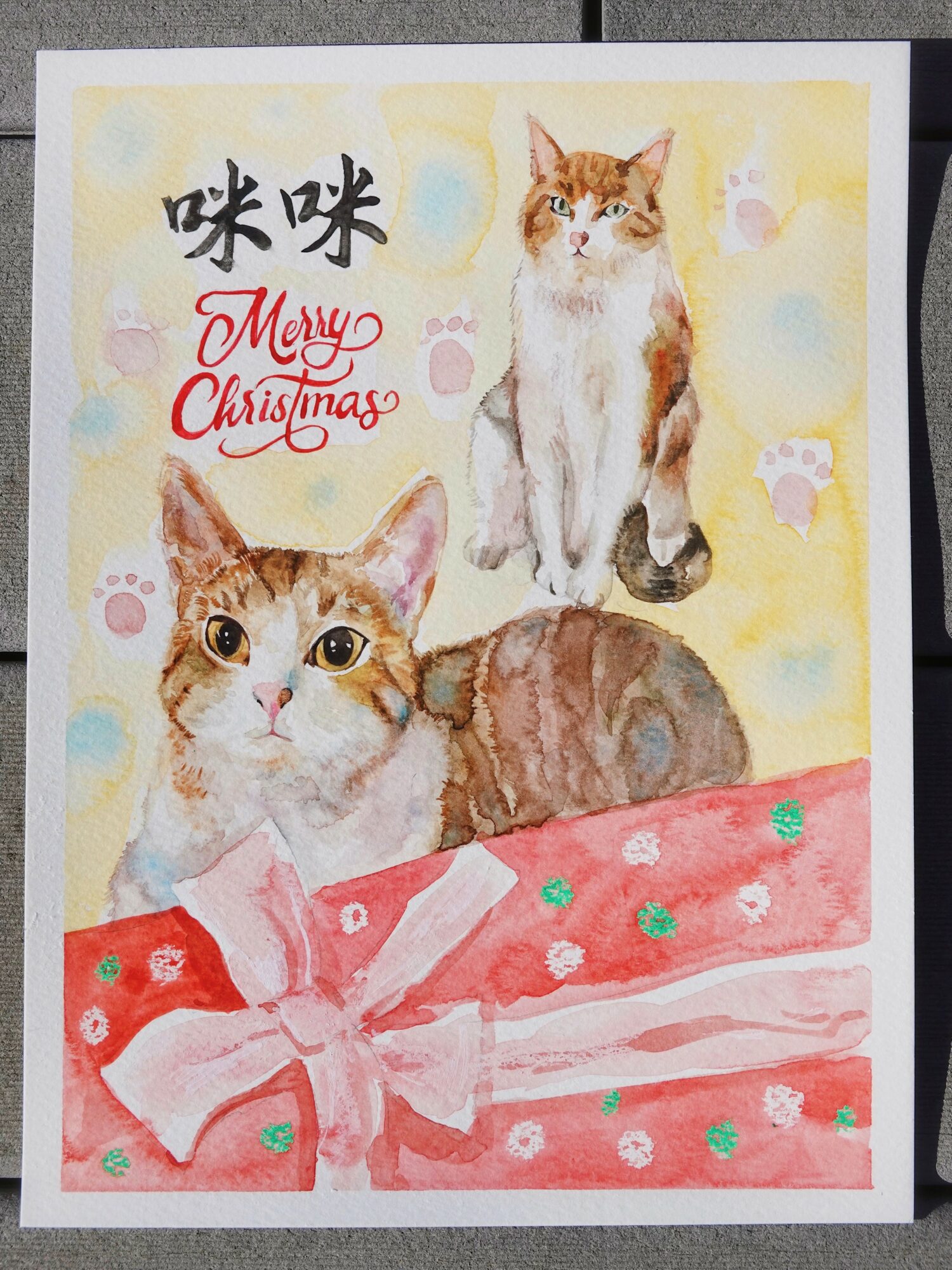 Watercolor Christmas card with two cats, a gift box, and festive background, with text in Japanese and English.