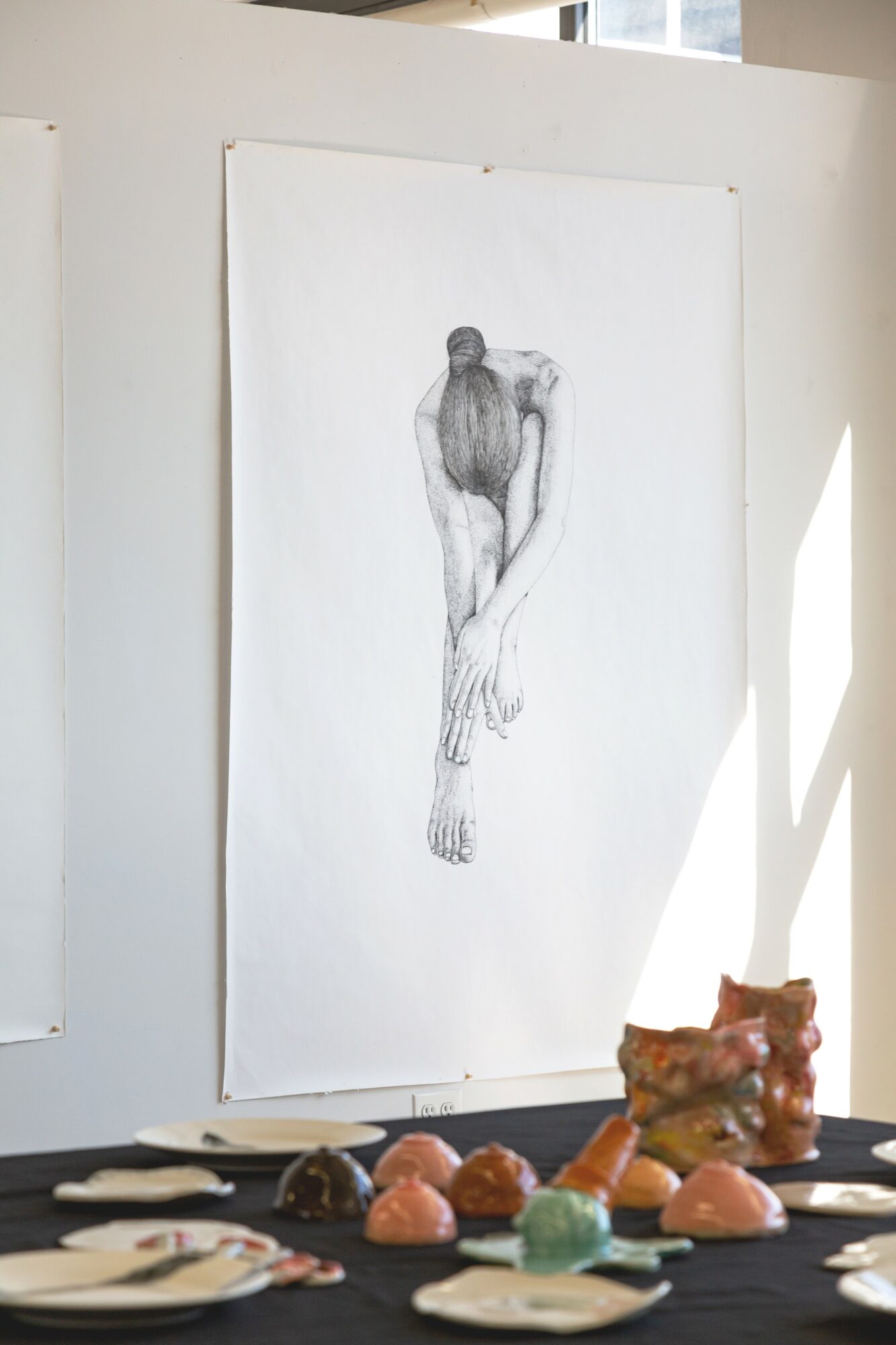 A pencil sketch of a person with their head down and arms hanging, displayed on a white wall.