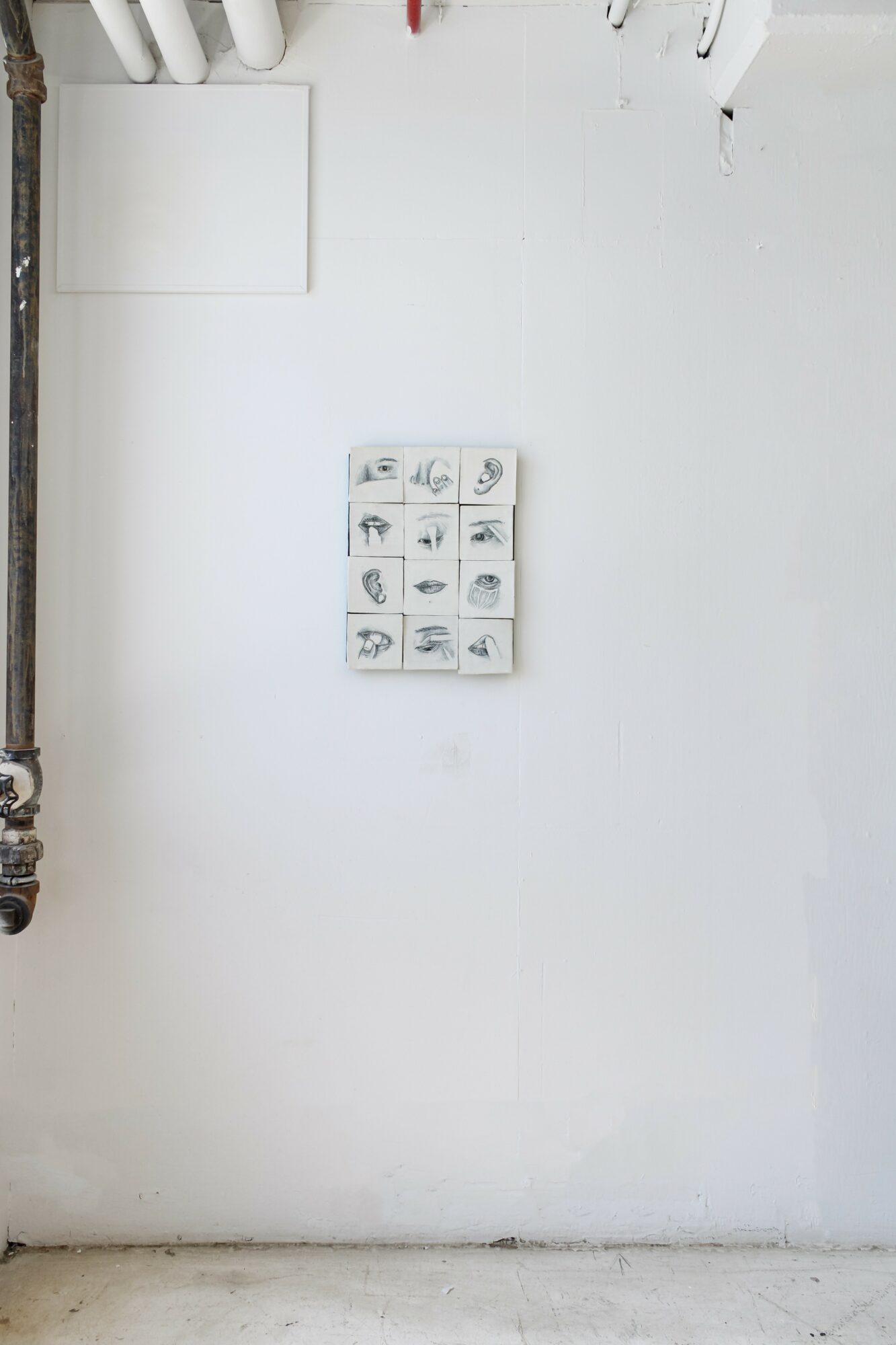 Small display with various objects on a white wall, with a pipe on the left side and hooks at the top.