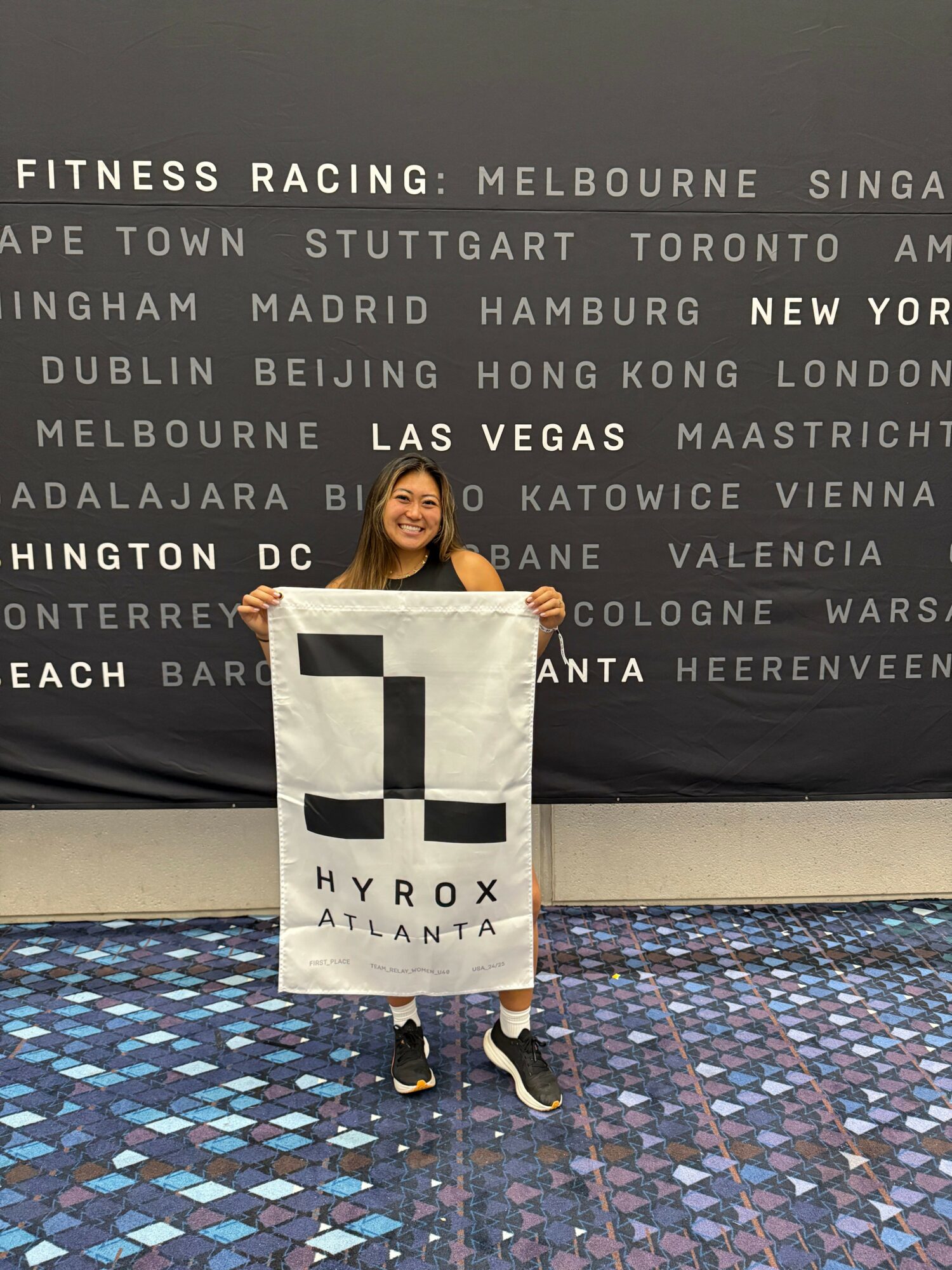 Person holding a large check with a geometric design, standing on a colorful tiled floor, with a black and white text background behind them.