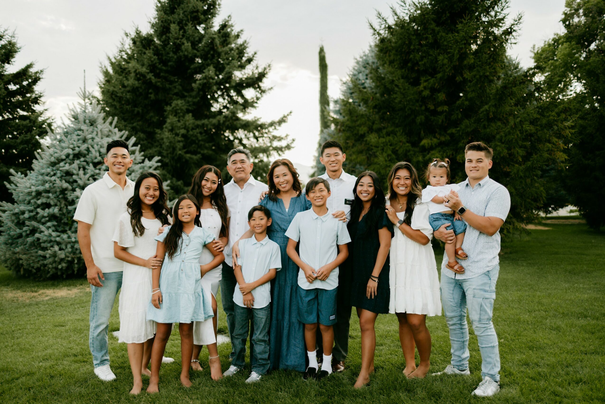Group of people standing outdoors on grass, with trees in the background, smiling for a photo.