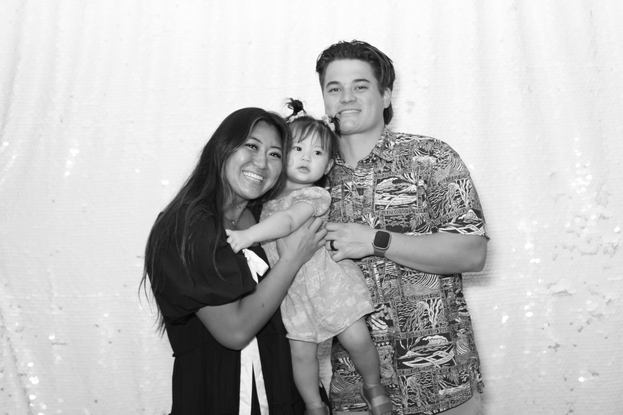 Three people, a woman, a man, and a child, smiling and posing together in front of a curtain, black and white photo.