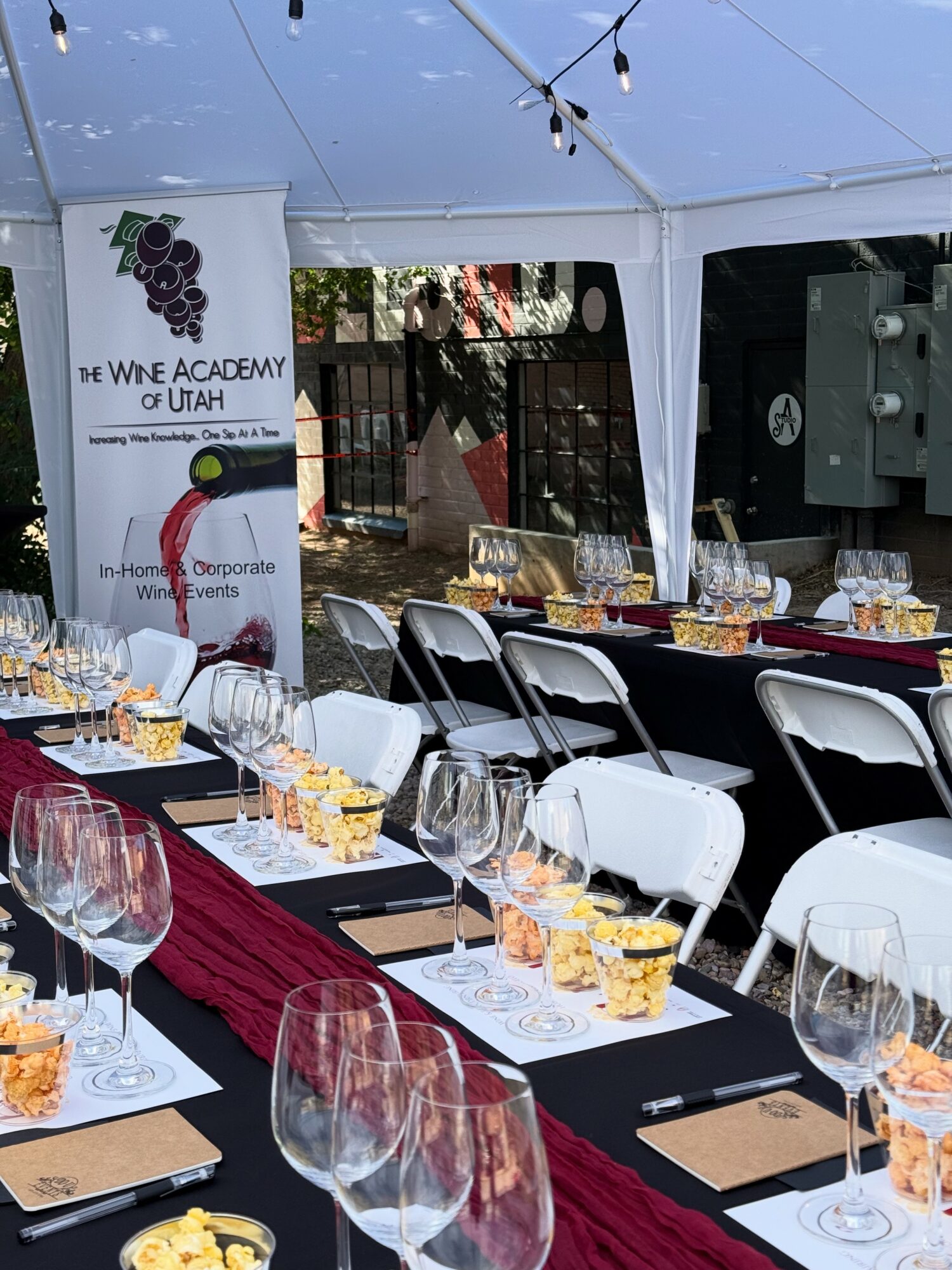 Event setup with tables, chairs, and glassware inside a tent, with a banner for the Utah Wine Academy visible.