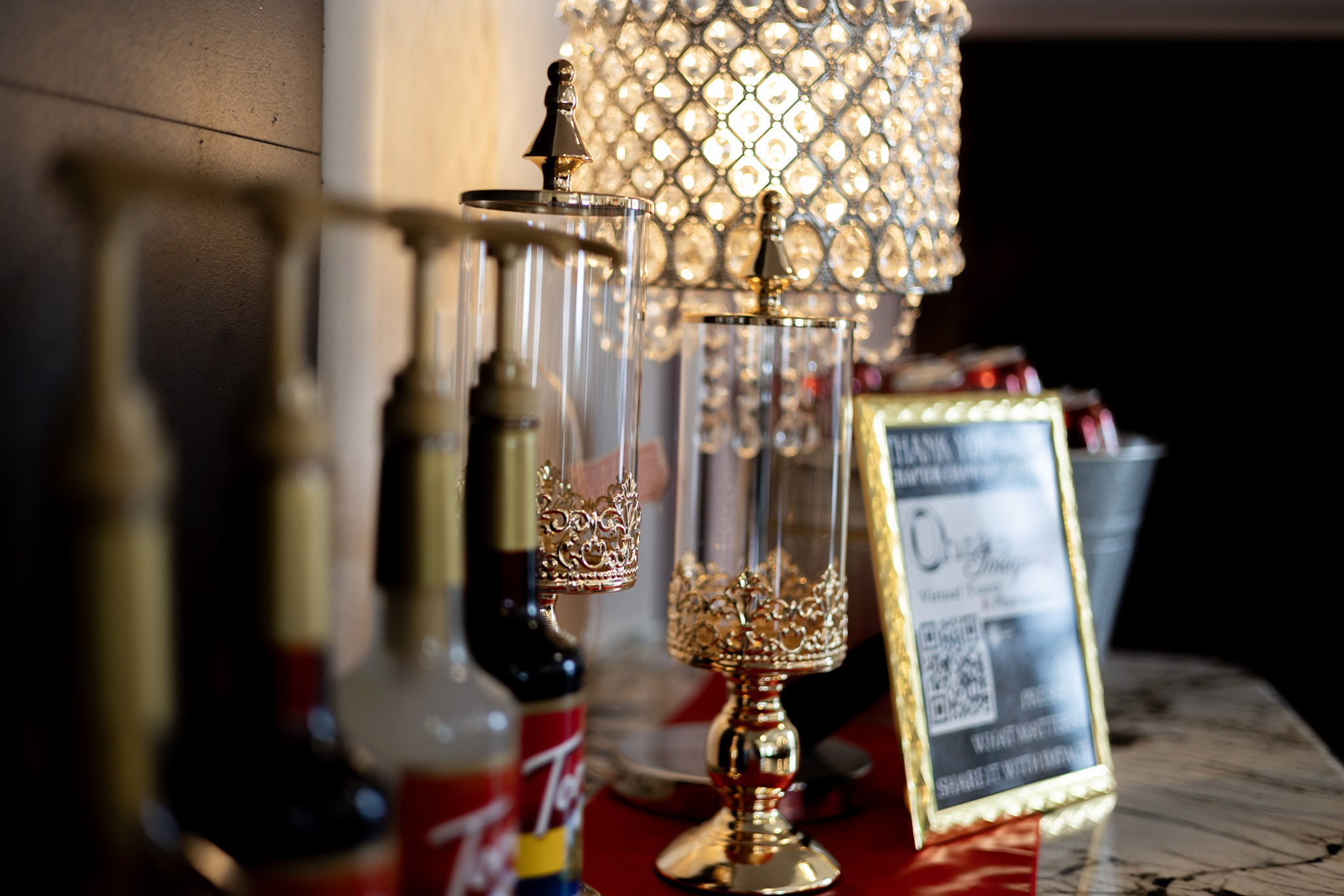 Decorative lamps, glassware, and a framed menu on a marble surface, with warm lighting and a dark background.
