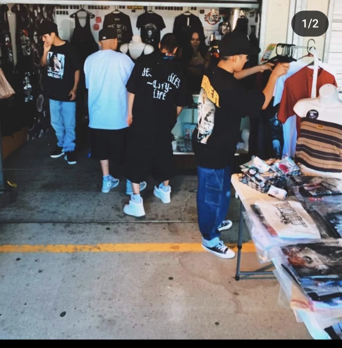 People shopping at an outdoor market with clothing and accessories displayed on tables and racks.